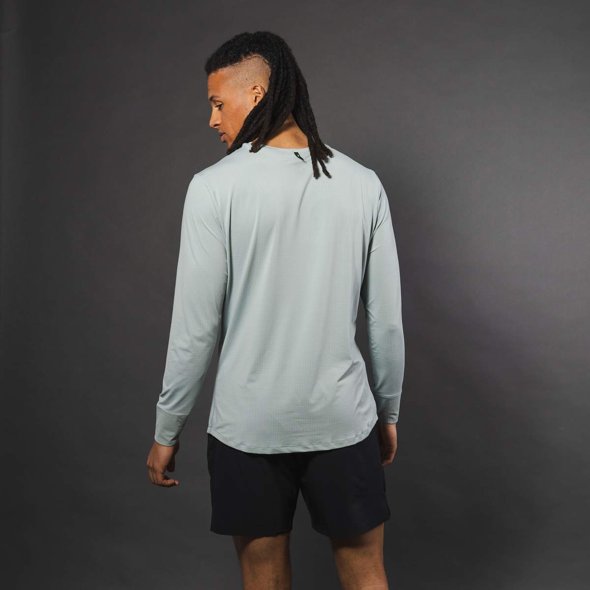 Light gray men's long sleeve performance shirt with micro-perforated texture, back view, worn with black shorts