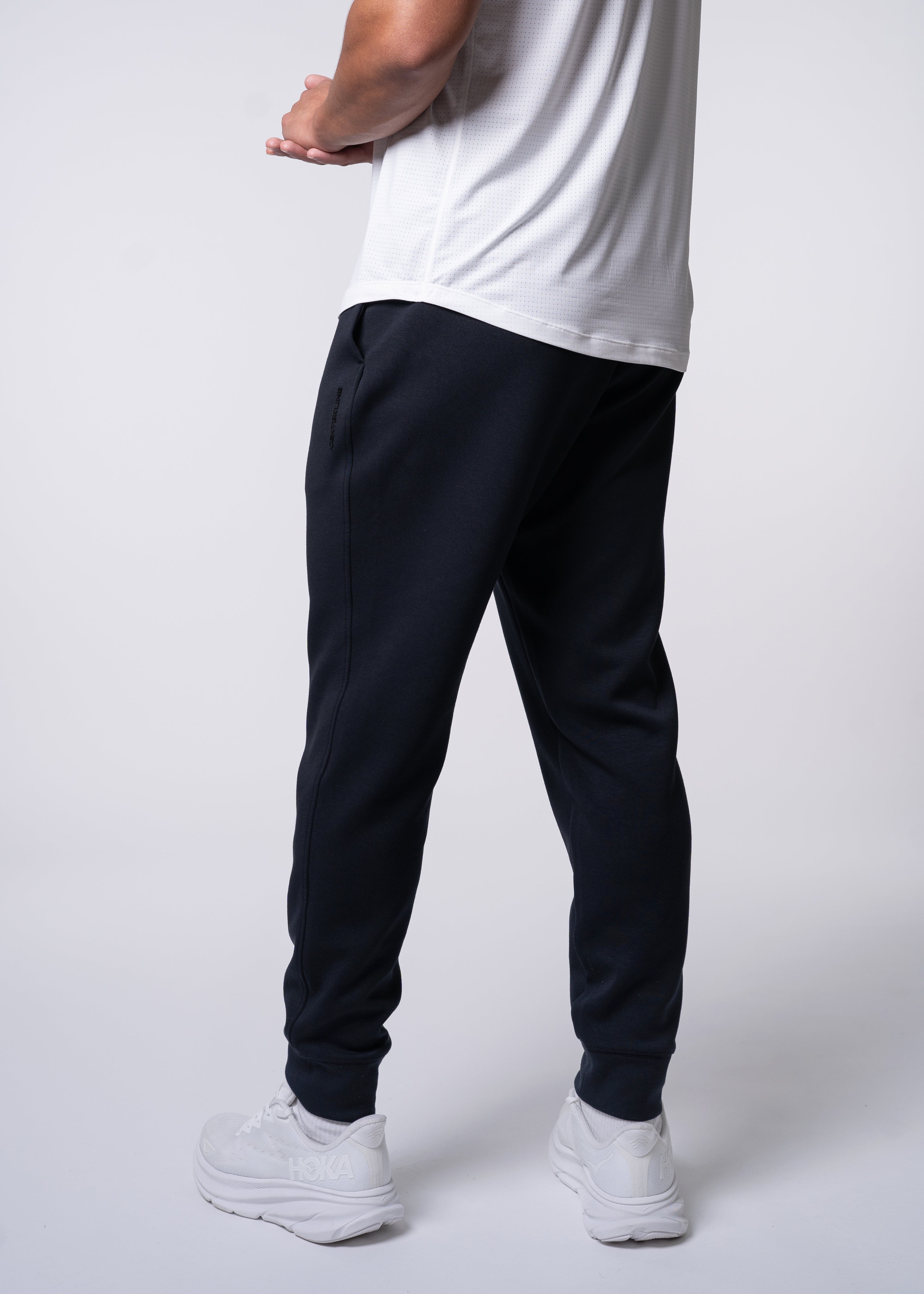 Rear view of a person wearing a white t-shirt, black sweatpants, and white sneakers.