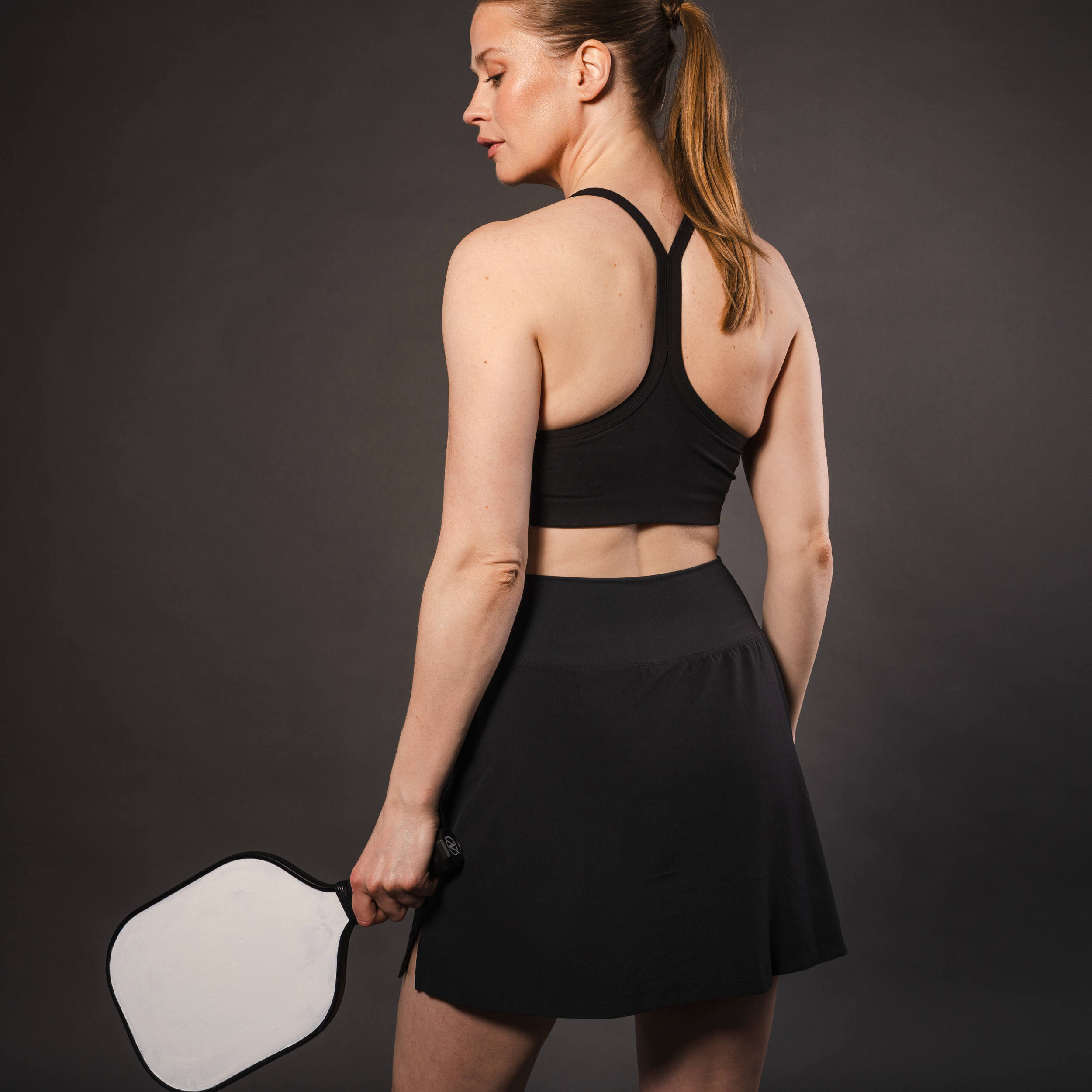 Woman in black athletic clothing holding a pickleball paddle.