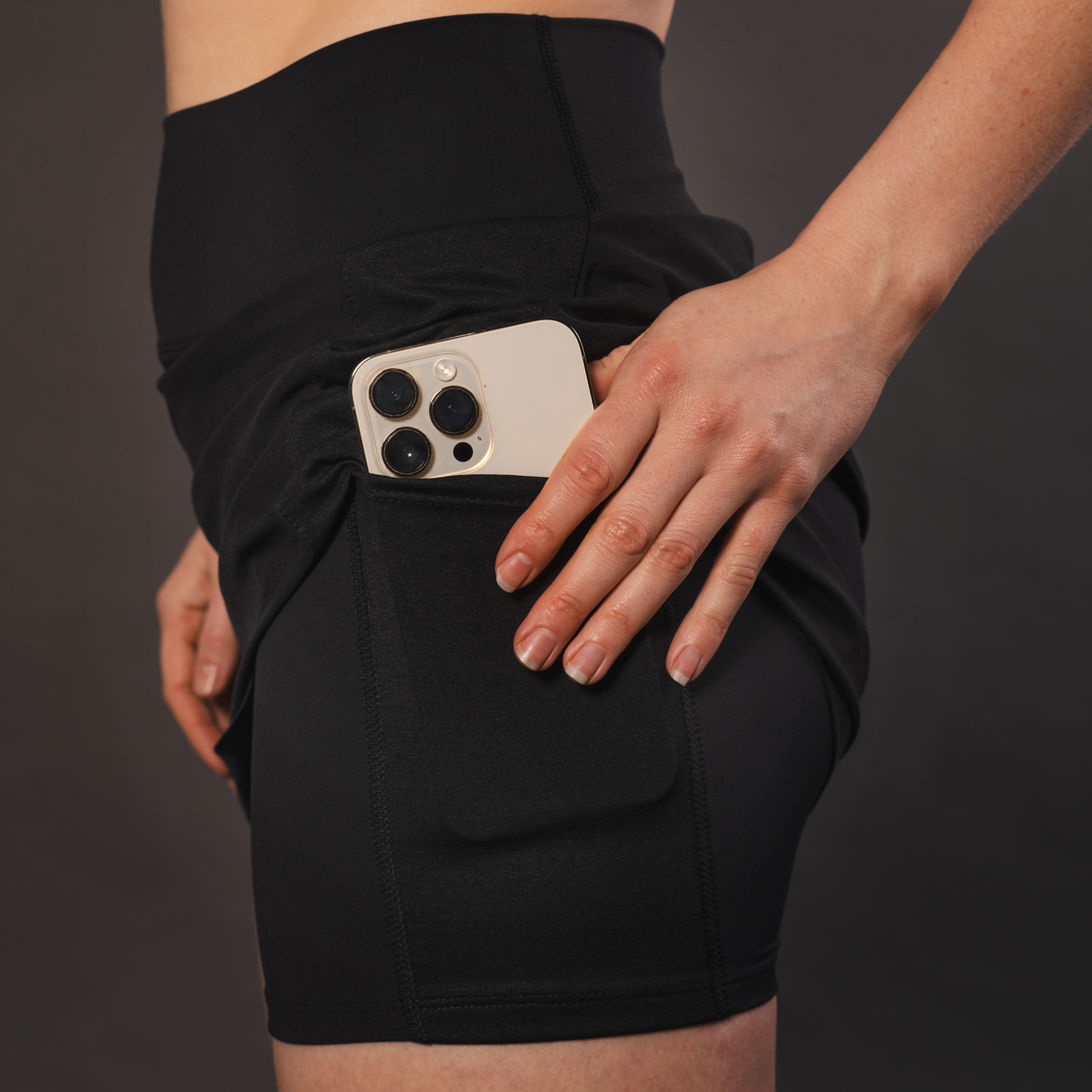 Black athletic shorts with built-in pockets holding a smartphone, against a gray background.