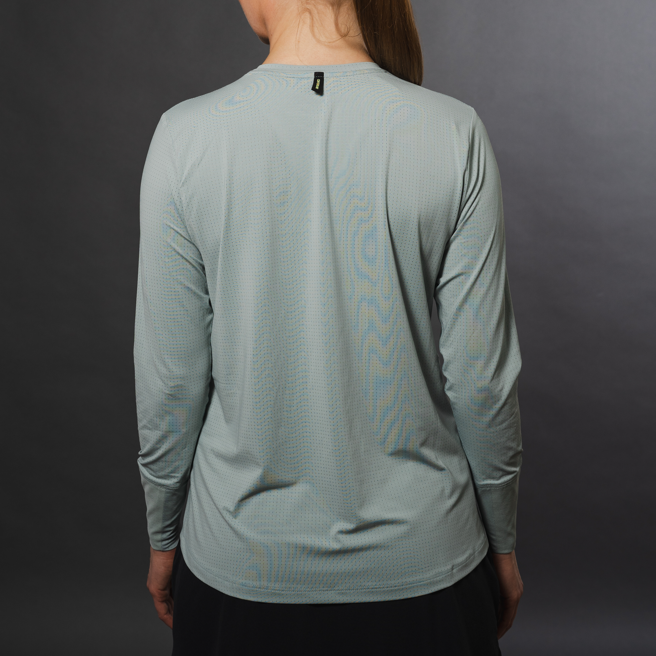 Woman in a gray long-sleeved perforated shirt, rear view, against a gray backdrop.