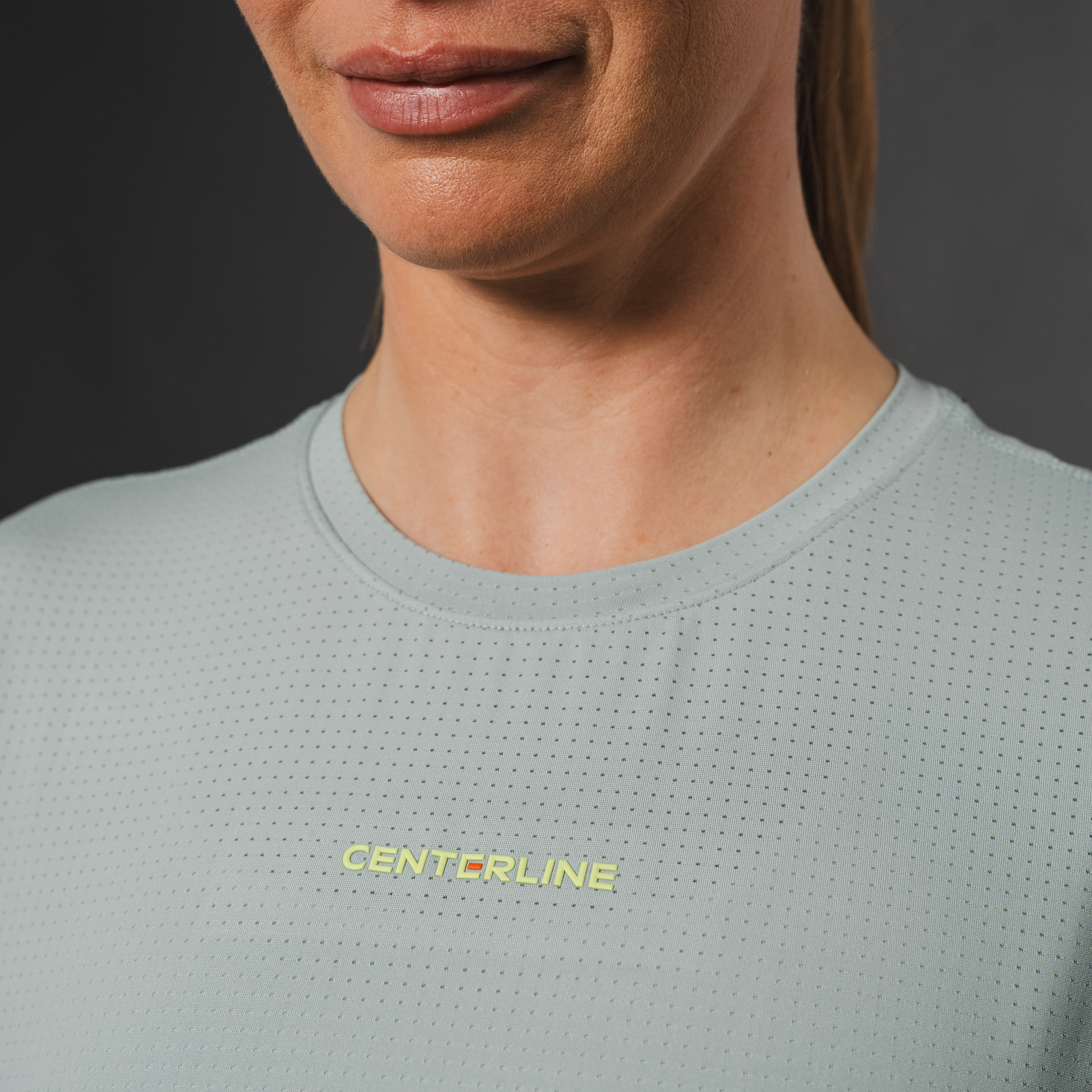 Close-up of a woman wearing a light gray, perforated athletic shirt with "CENTERLINE" in yellow text.