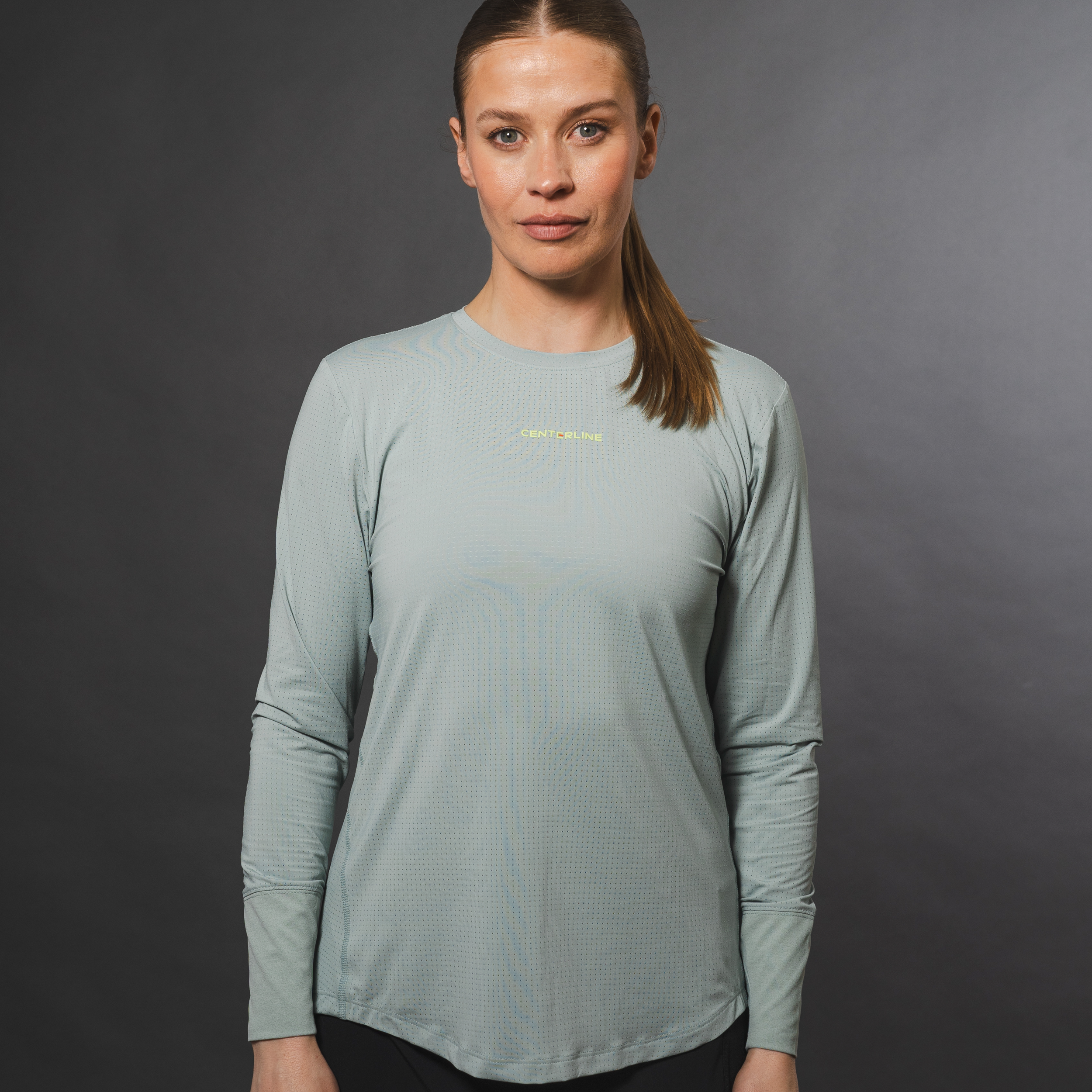 Woman wearing a long-sleeved gray shirt with a dotted texture and the word "CENTERLINE" on the chest, posed against a gray background.