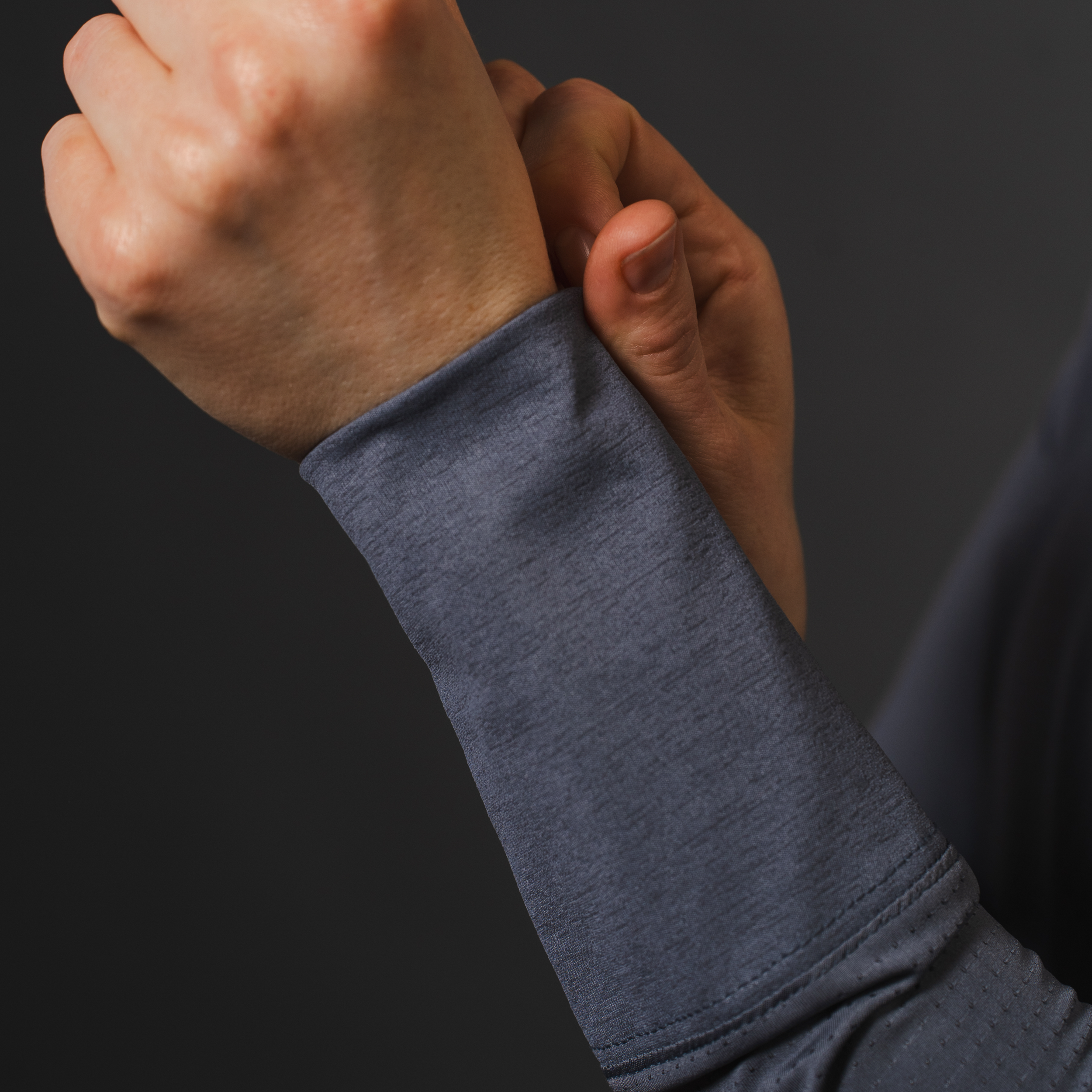 Person holding their left wrist with their right hand; gray athletic shirt.