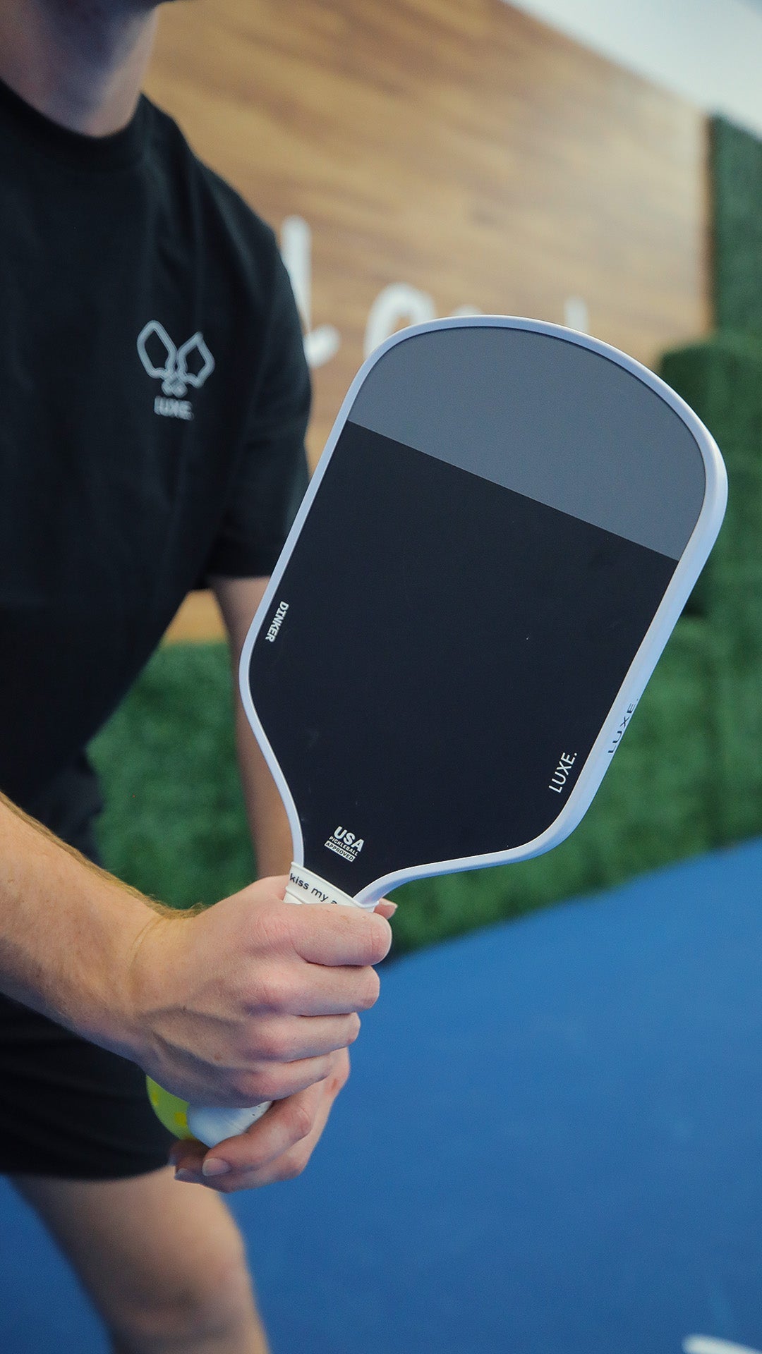 Person holding a black and gray Luxe pickleball paddle on a blue court.