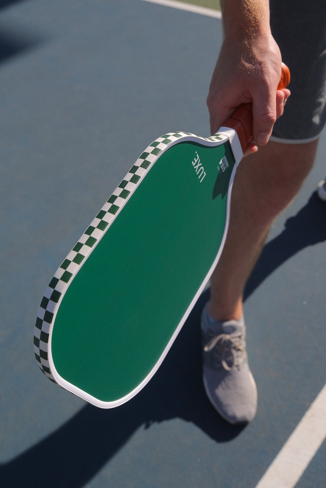 Man holding a green pickleball paddle with checkered edge, standing on a blue court.