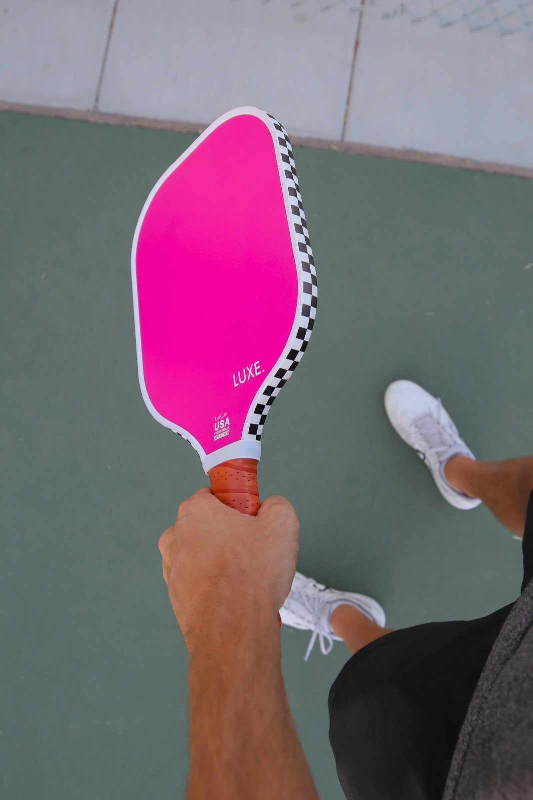 A person holding a pink pickleball paddle with a checkered pattern.