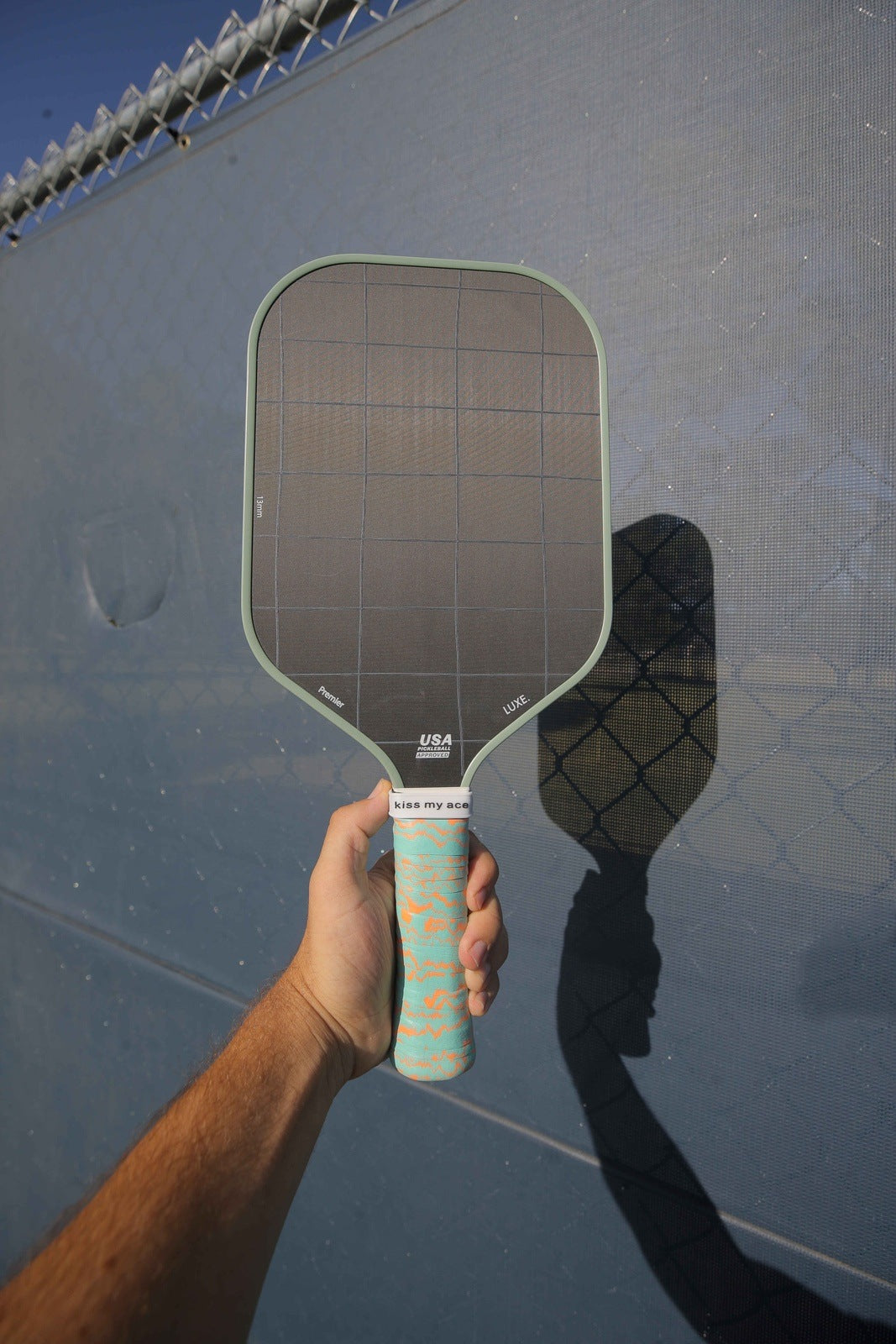 Hand holding a green and orange pickleball paddle with shadow.