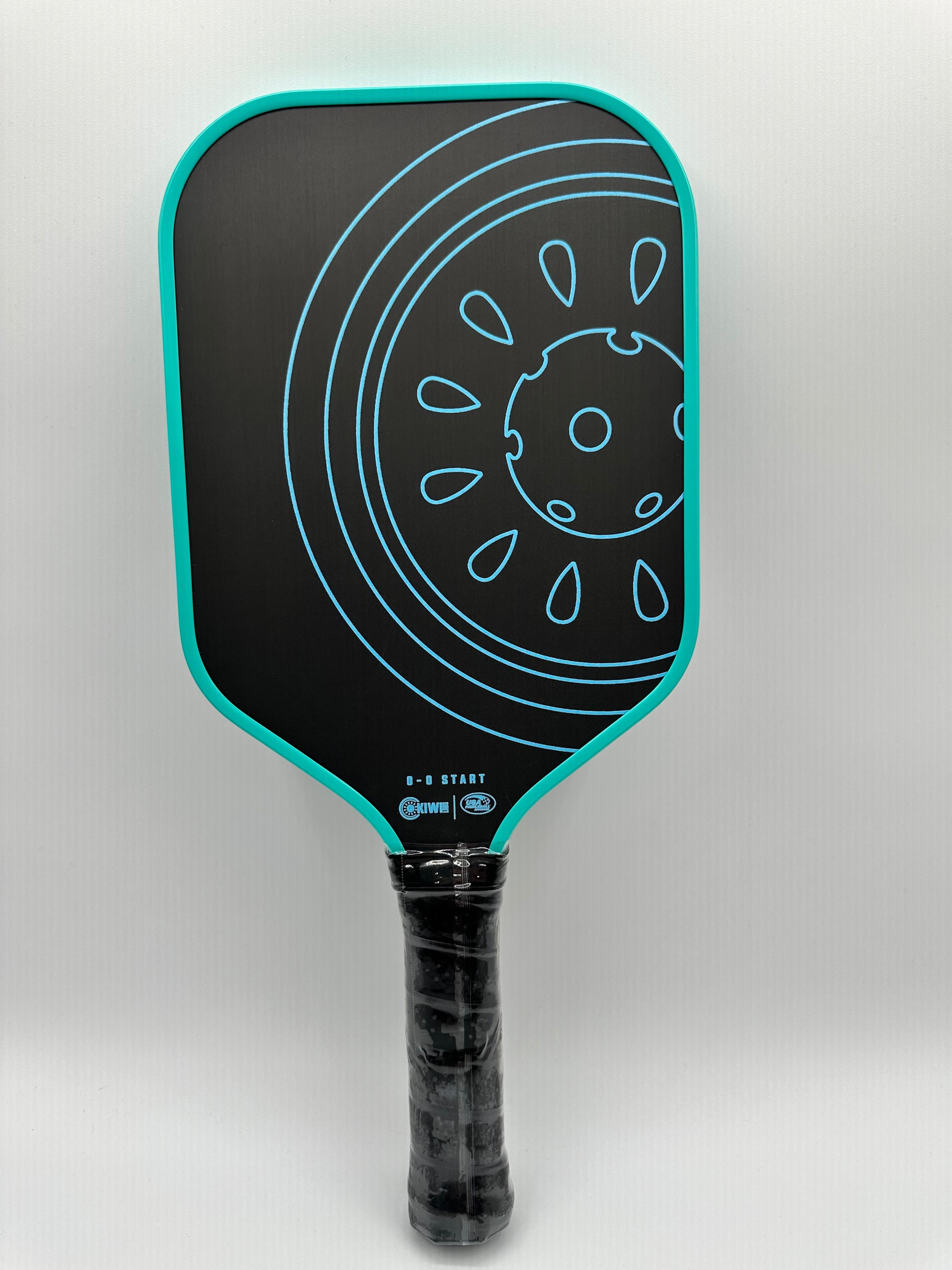 Black pickleball paddle with teal trim and a teal concentric circle design.