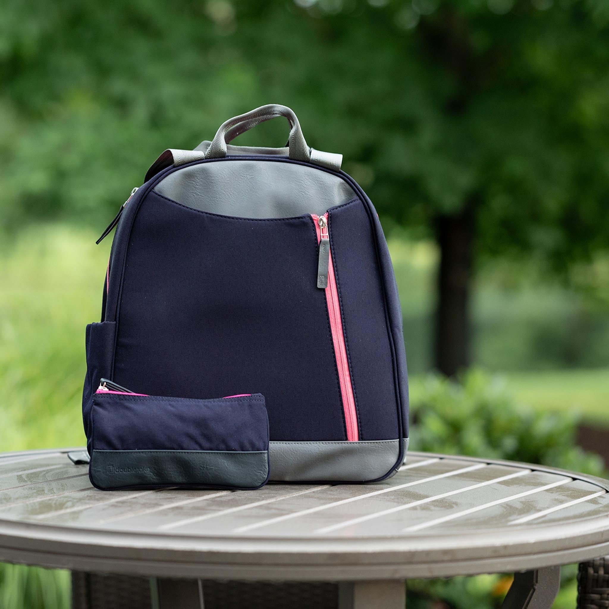Navy and grey pickleball backpack and matching tote by Doubletake, featuring vibrant pink zippers, on an outdoor table.
