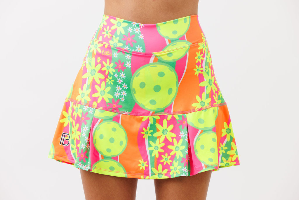 Vibrant drop pleat skort by Pickleball Bella, with neon green, pink, orange, daisy, and pickleball print.