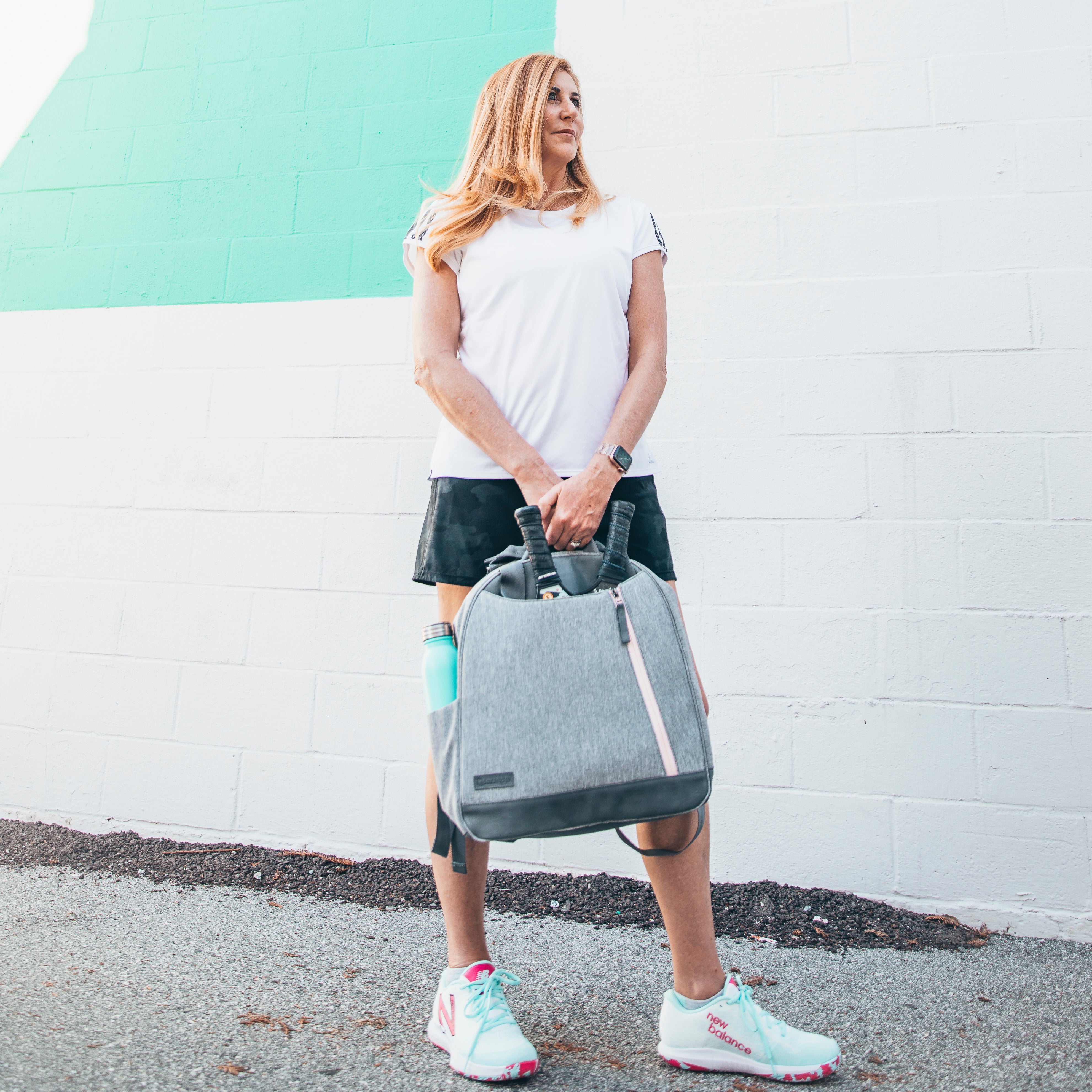 Heather gray pickleball backpack and tote by Doubletake with pink zipper accents, held by a woman.