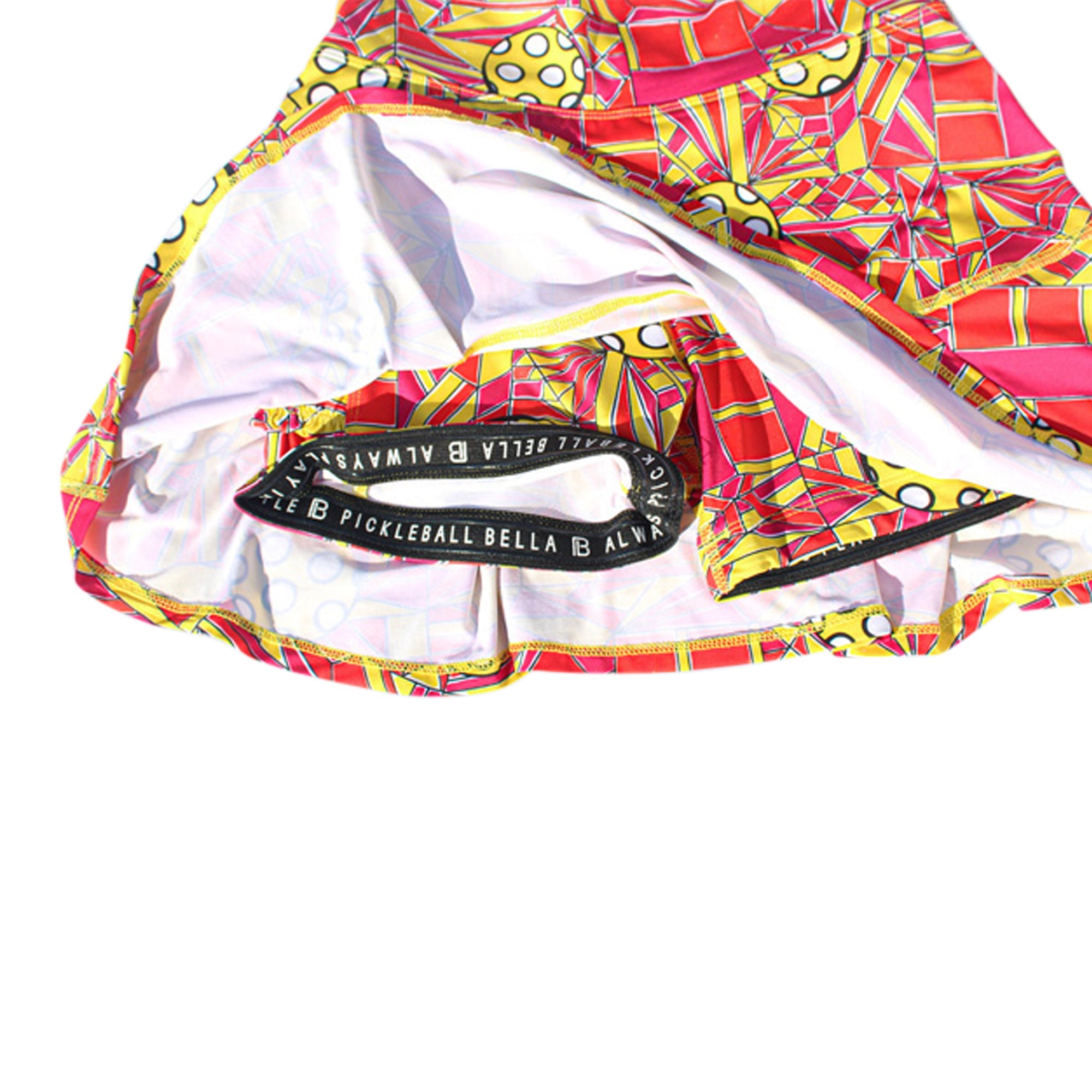 Red, yellow, and pink pickleball pattern pleat skort by Pickleball Bella, revealing inner white shorts with a branded elastic waist.