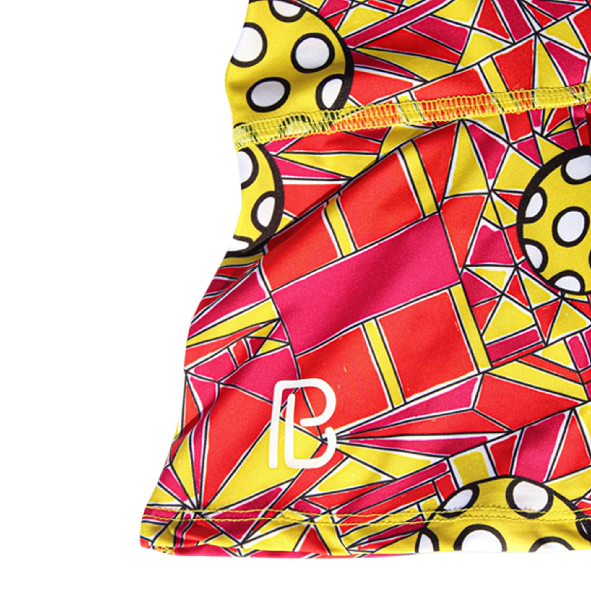 Red, yellow, and pink pleat skort by Pickleball Bella with geometric stained glass and pickleball patterns, featuring a white PB logo.