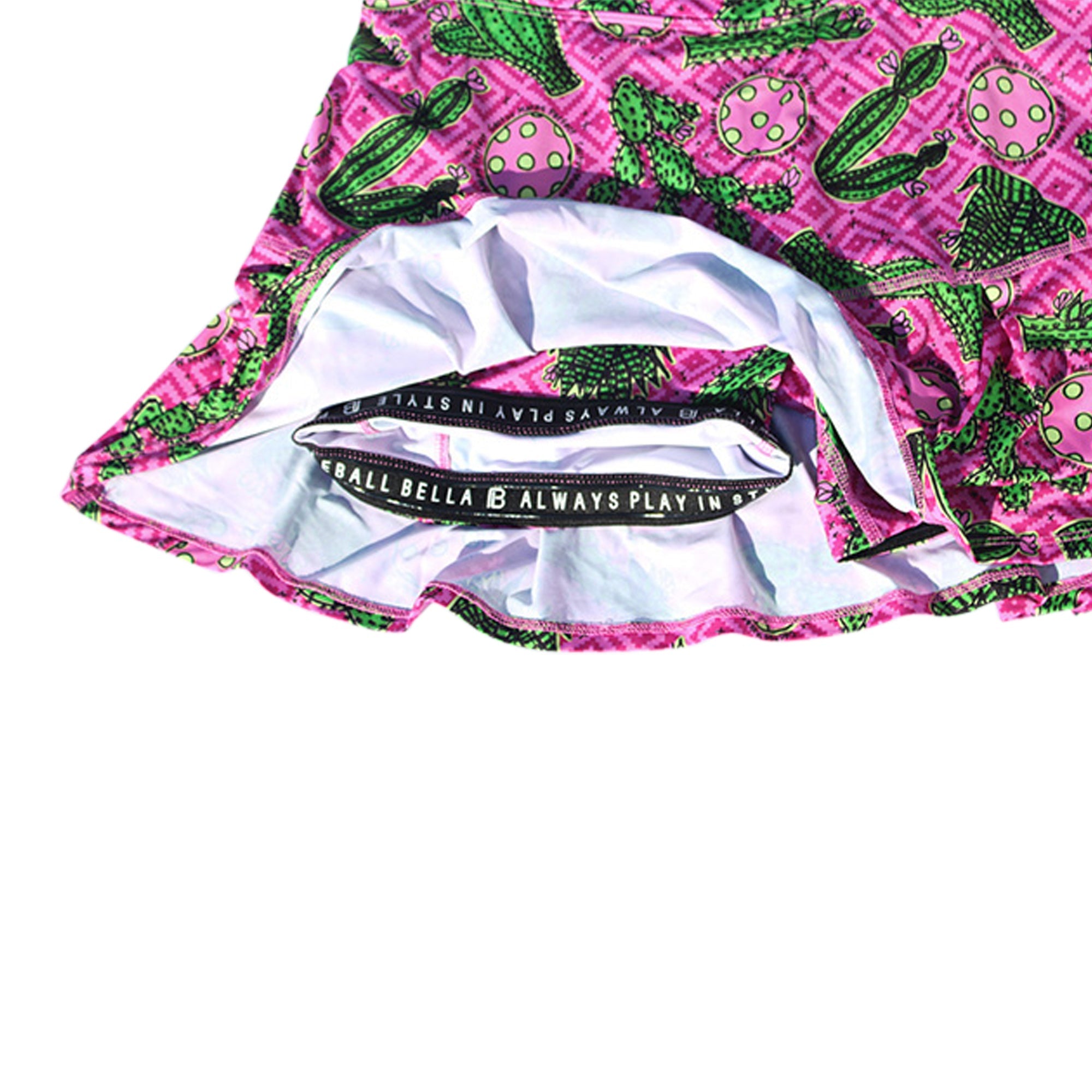 Pleat Skort in pink with green cactus pattern by Pickleball Bella, revealing white inner shorts and a black logo waistband.