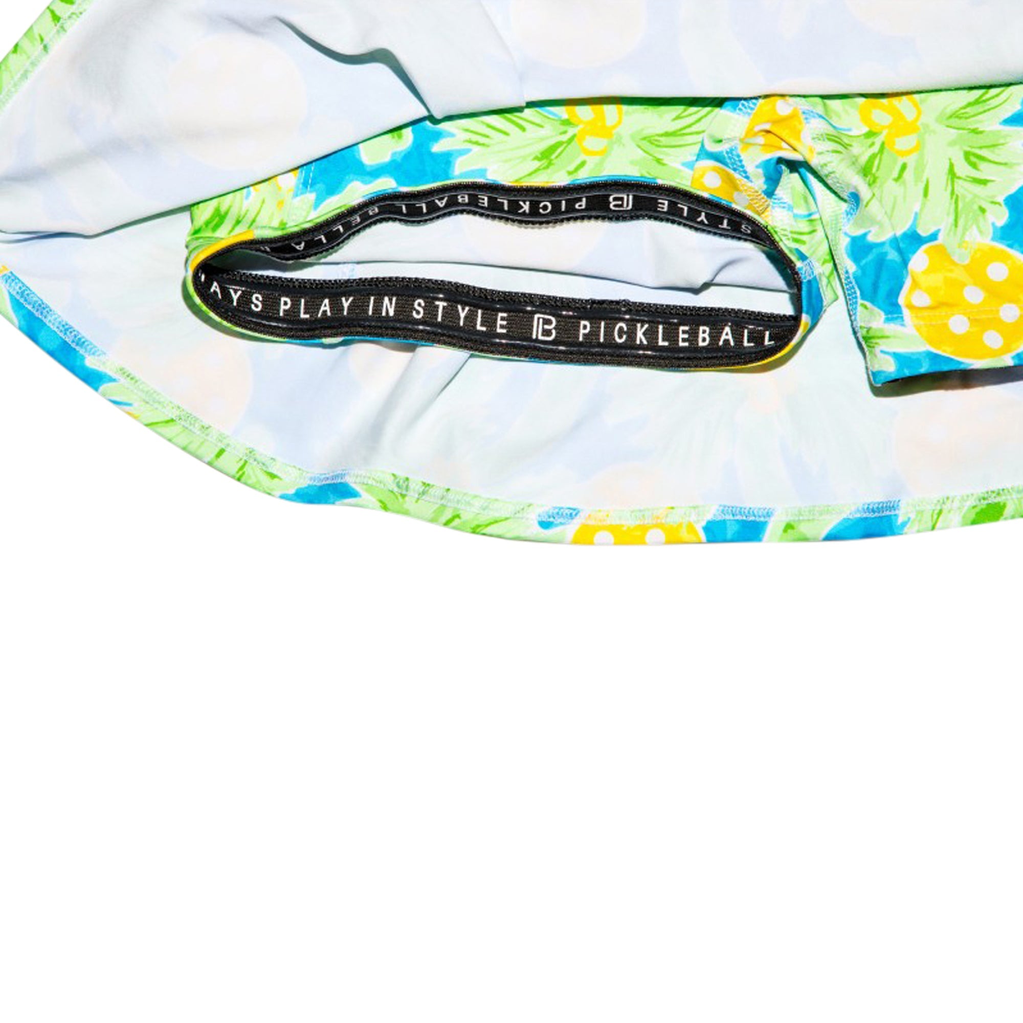 Blue, green, and yellow tropical print pleat skort by Pickleball Bella, with a visible inner black waistband text and polka dot details.
