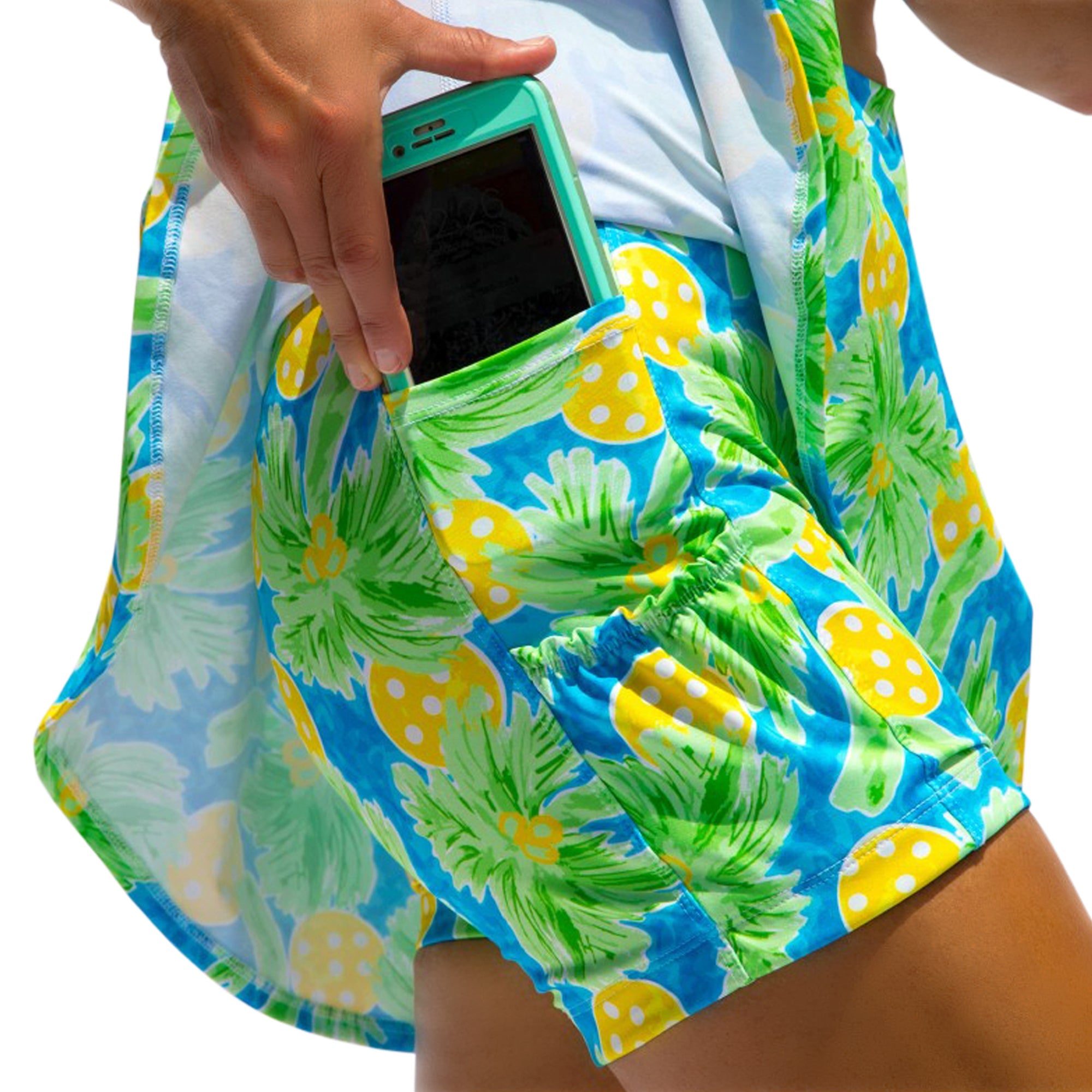 Blue, green, and yellow patterned pleat skort by Pickleball Bella, featuring tropical palms and polka dots, with a phone in its side pocket.