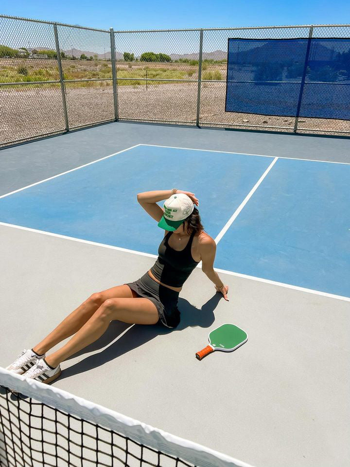 Woman in athletic wear sitting on a pickleball court with a green paddle.