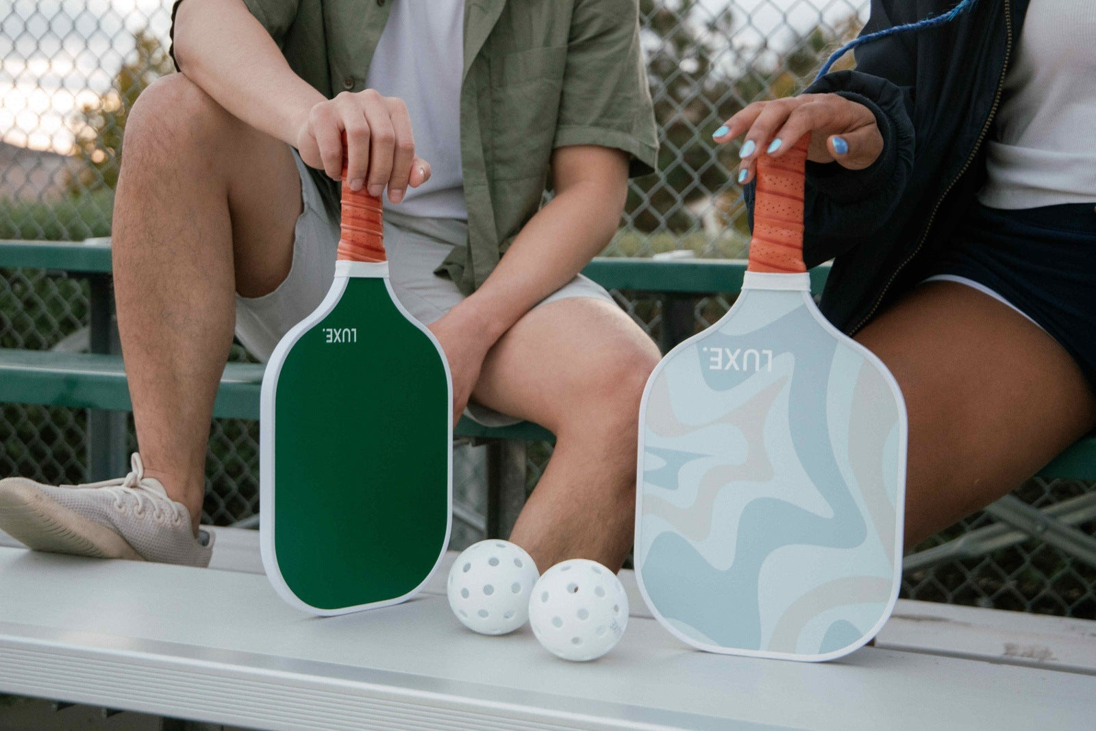 Two people sitting on a bench holding pickleball paddles.