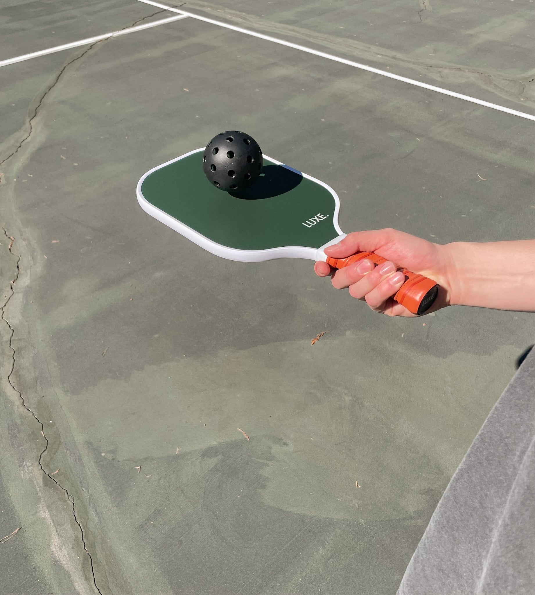 Hand holding pickleball paddle with ball on pickleball court.