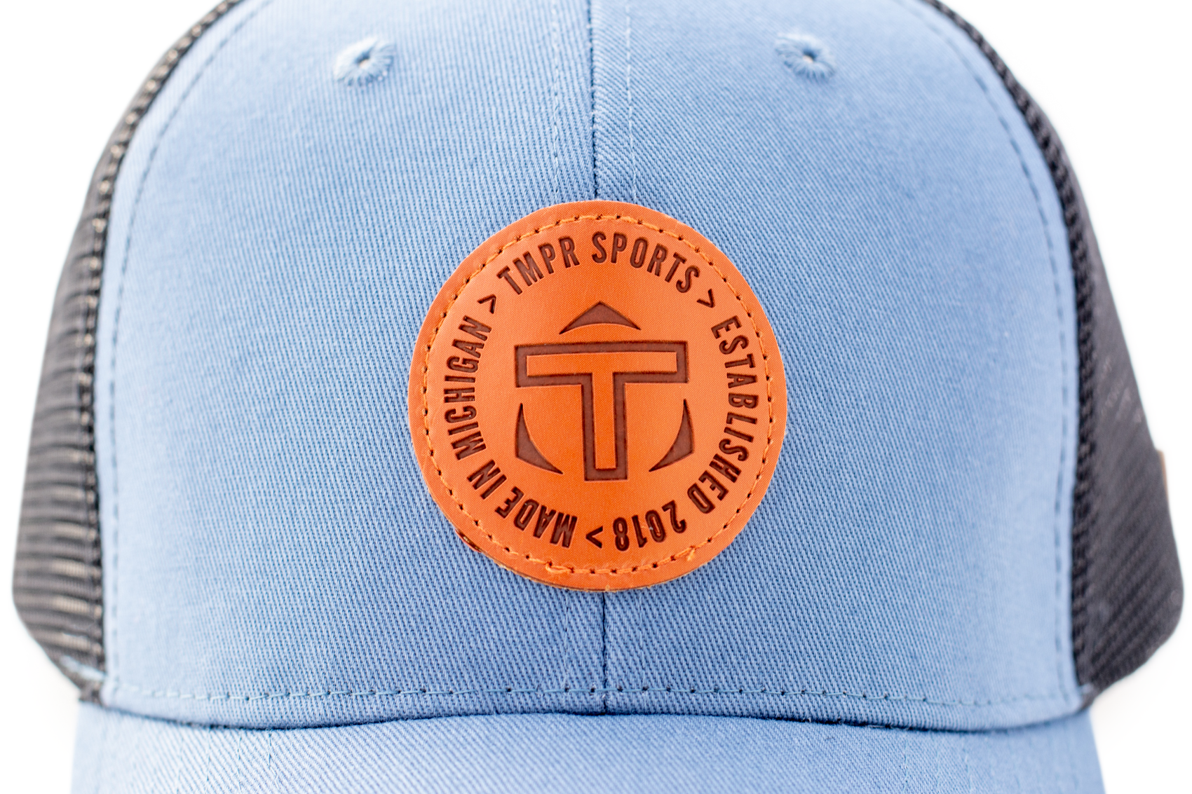 Light blue and dark gray trucker cap by TMPR Sports with a circular orange patch embossed with 'TMPR SPORTS', 'MADE IN MICHIGAN', 'ESTABLISHED 2018', and a stylized 'T'.