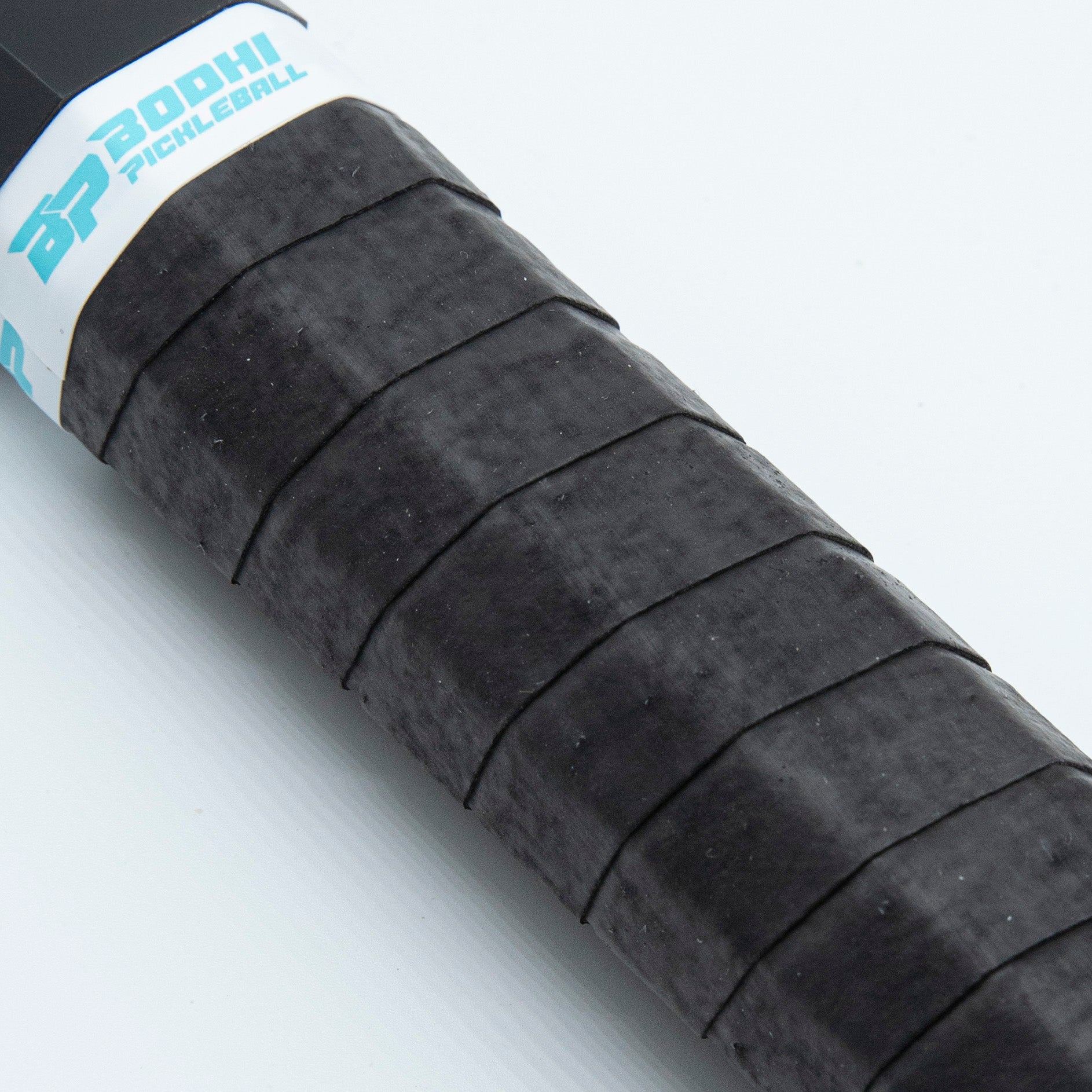 Close-up of a black, textured pickleball paddle handle with a white logo band.