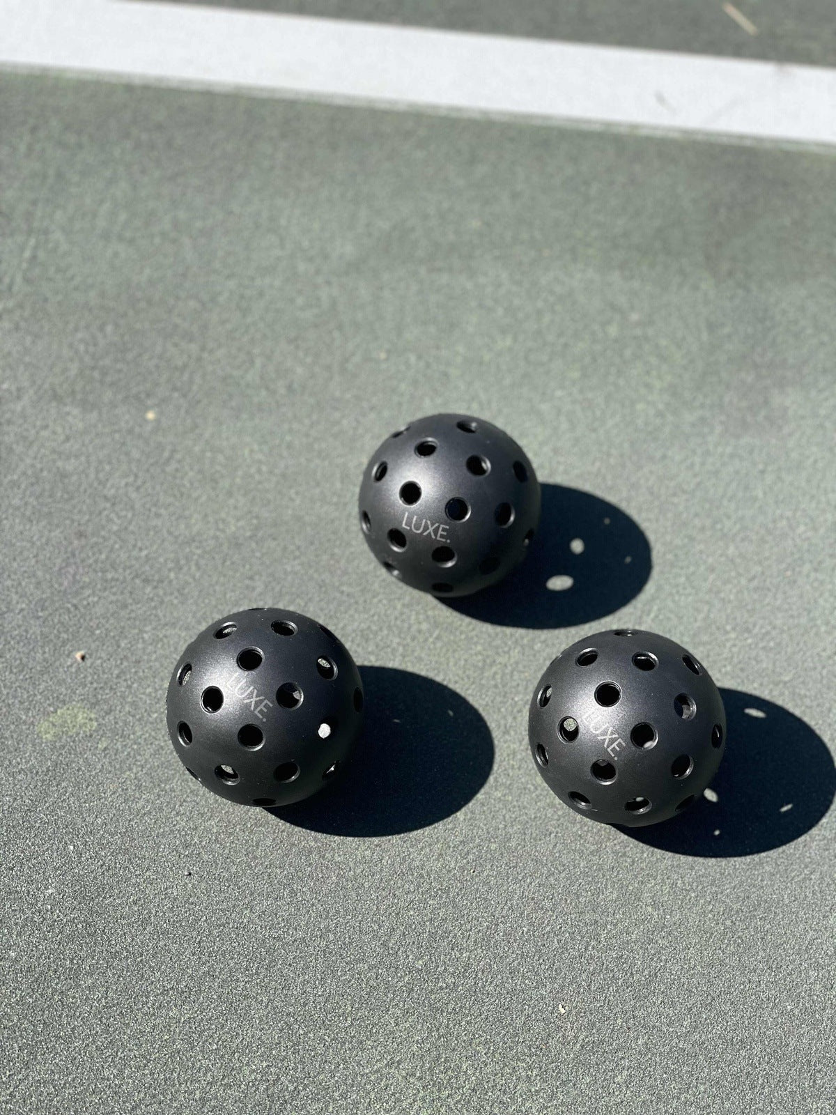 Three black pickleballs on a green court.