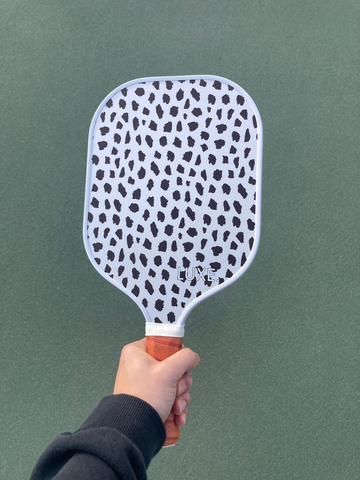 Hand holding a white pickleball paddle with black Dalmatian print.
