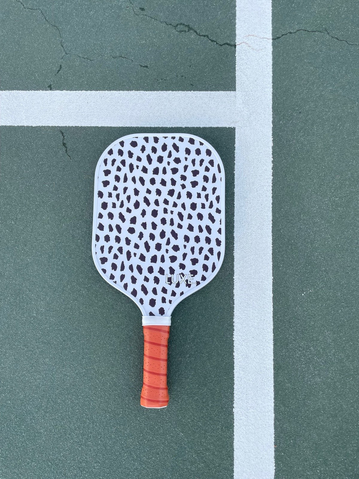 Pickleball paddle on green court, white with black cheetah print, orange grip.