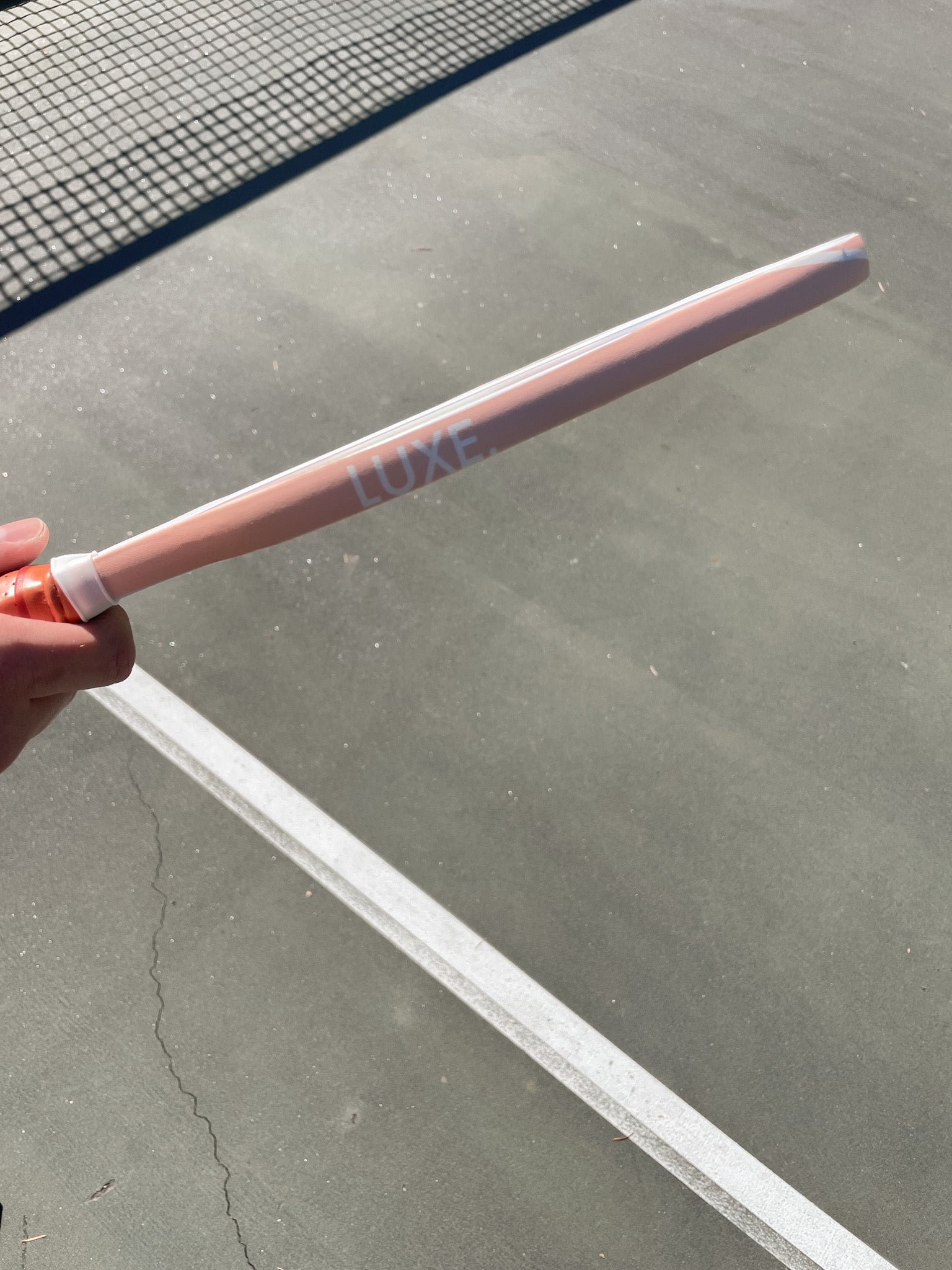 A pink pickleball paddle labeled "LUXE" held over a grey court with a white line.