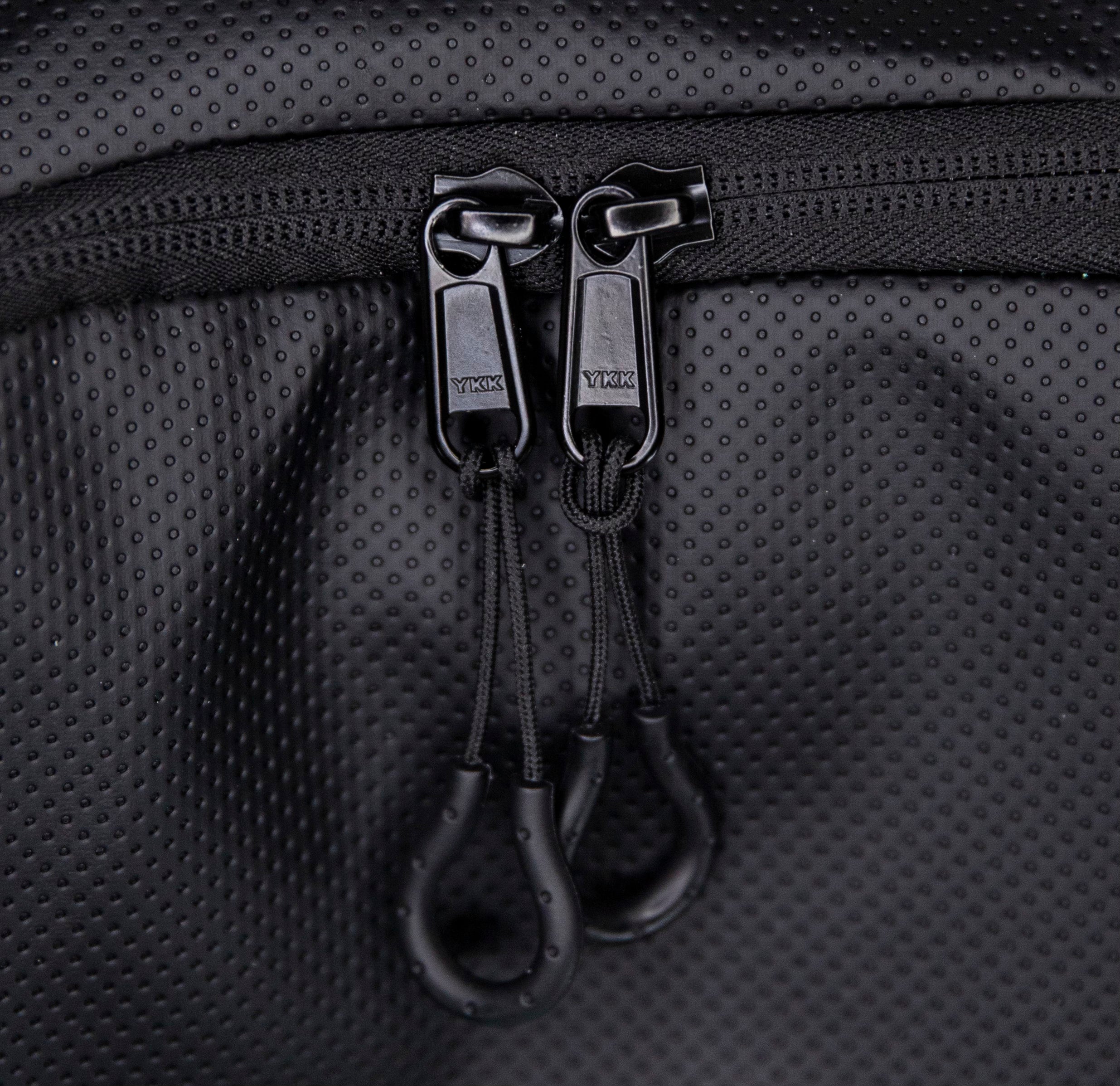 Close-up of black zipper with YKK pull tabs on textured material.