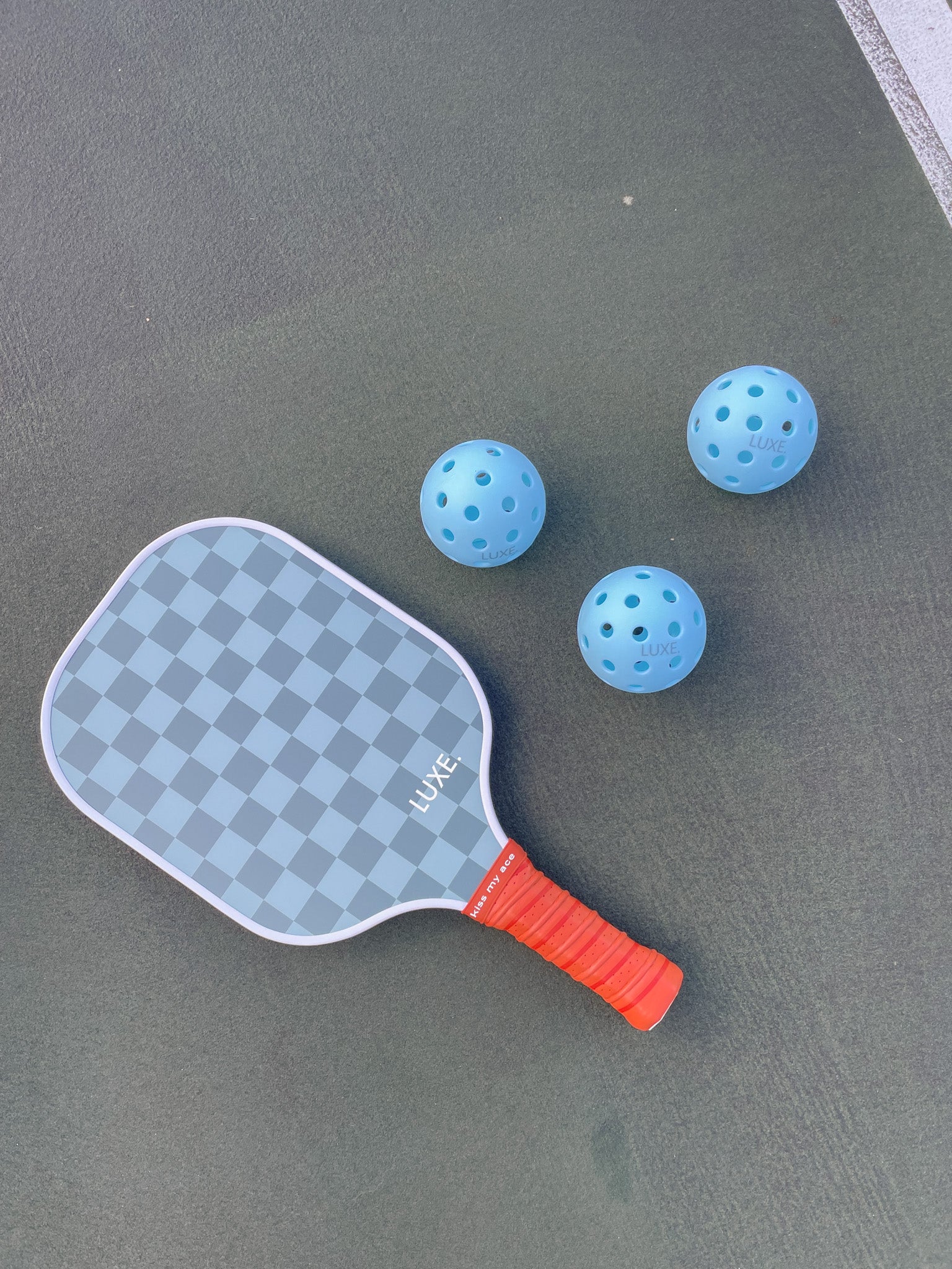 Pickleball paddle and three blue pickleballs on a gray court.