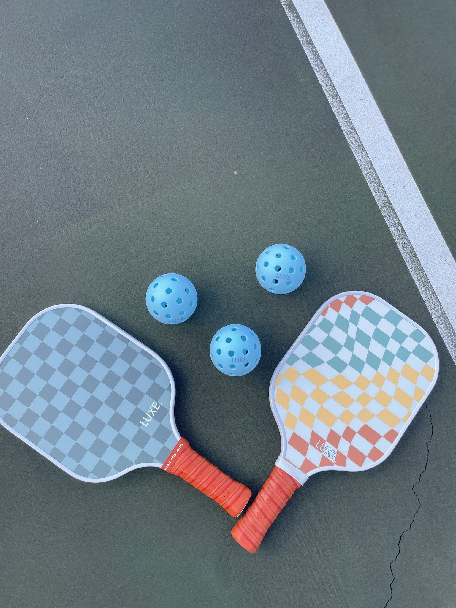 Overhead shot of pickleball paddles and balls on a green court with a white line.