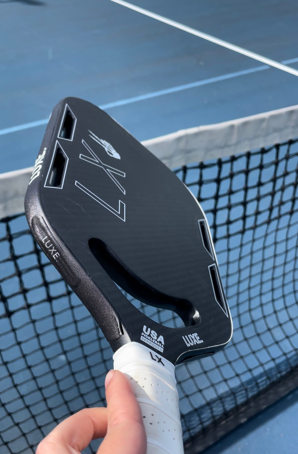 Black pickleball paddle with white grip on blue court.
