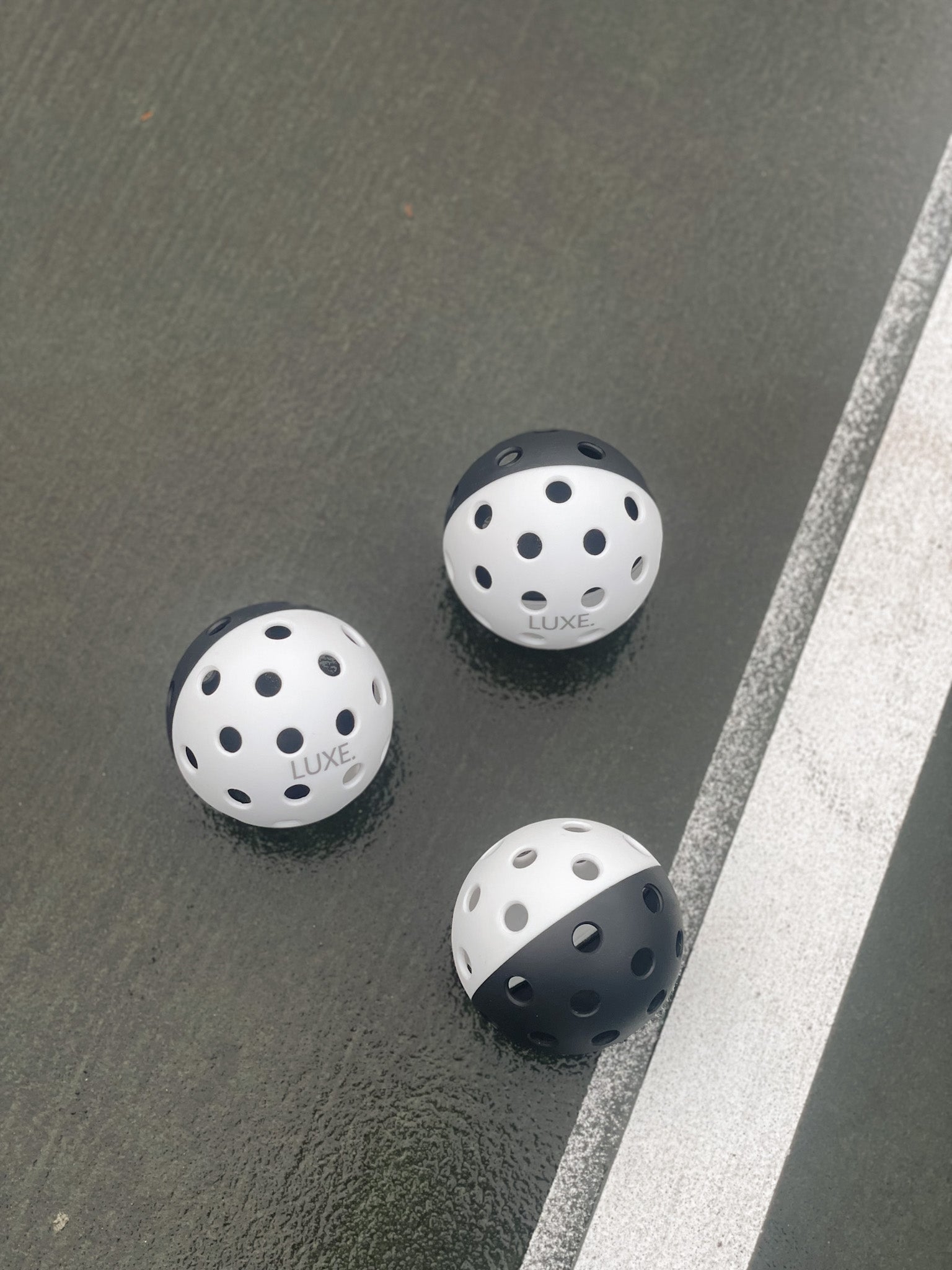 Three two-tone pickleballs on a gray court with a white line.