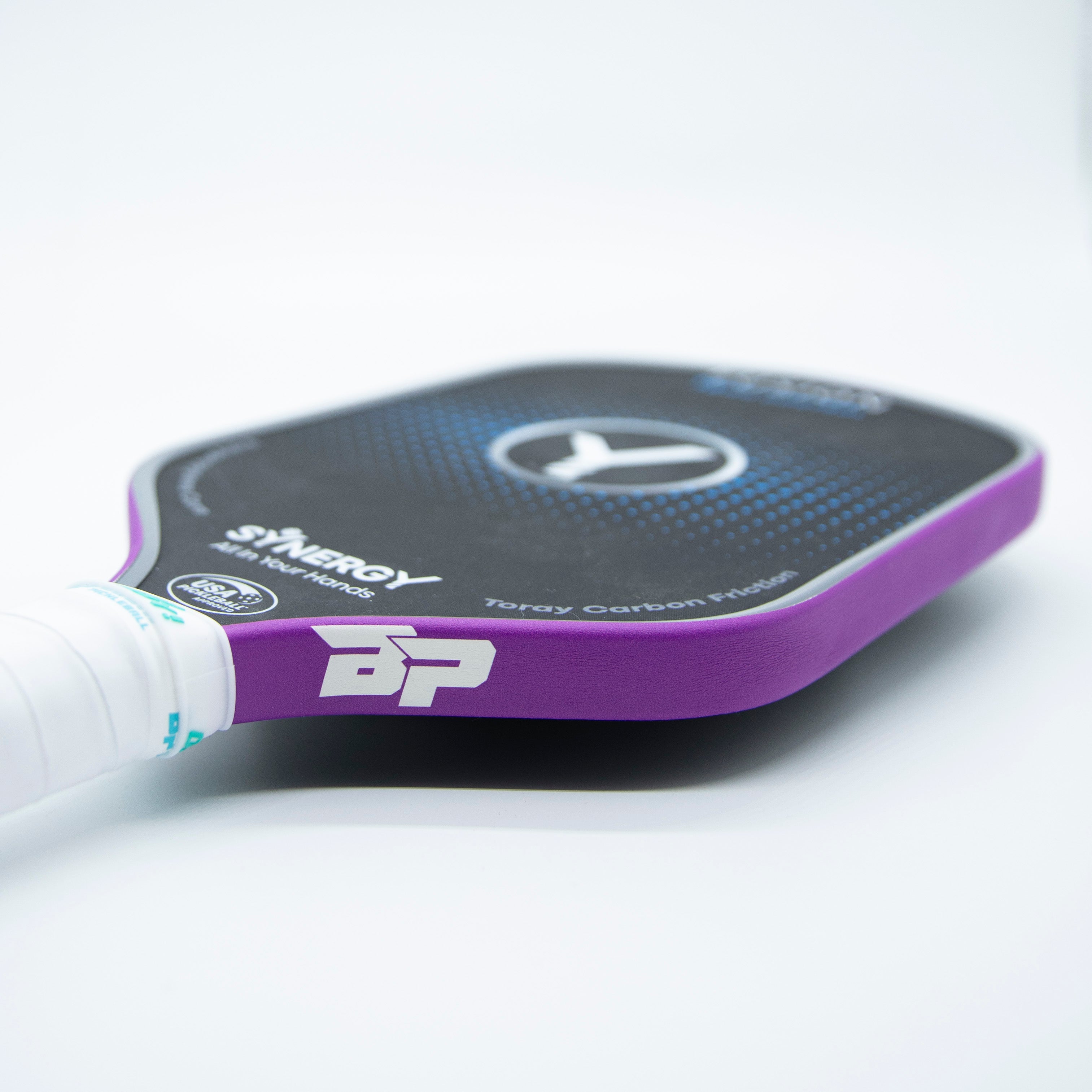 Purple Pickleball Paddle Edge Tape by DinkersAlley.com with white "BP" logo, on a black paddle with blue dots and a white grip, angled close-up.