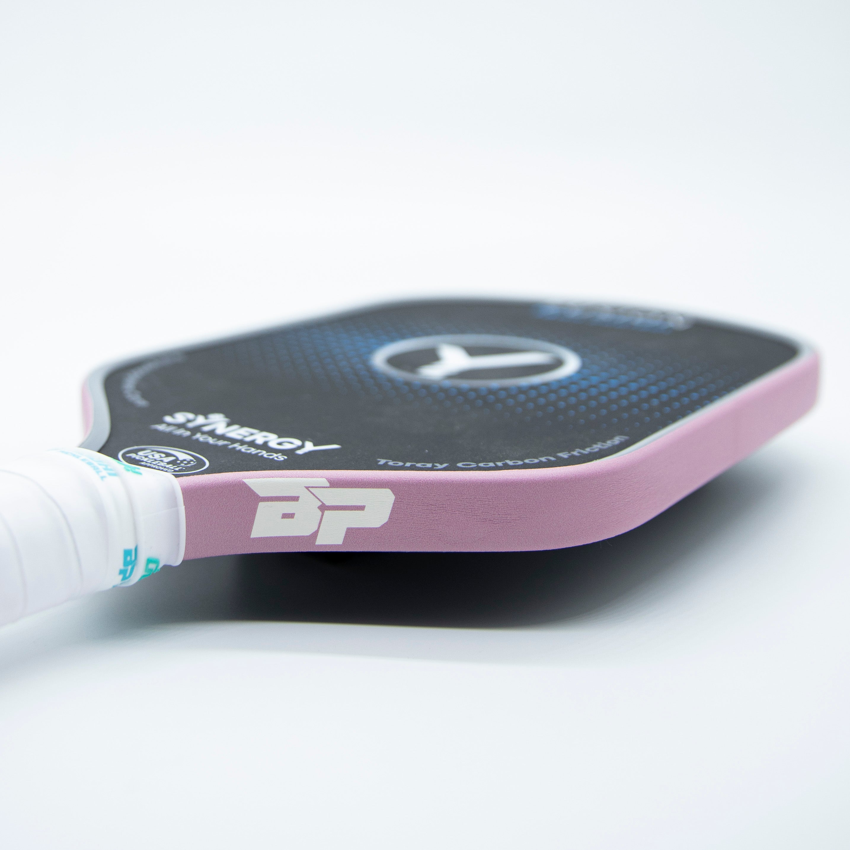 Textured light pink pickleball paddle edge tape by DinkersAlley.com applied to a black paddle.