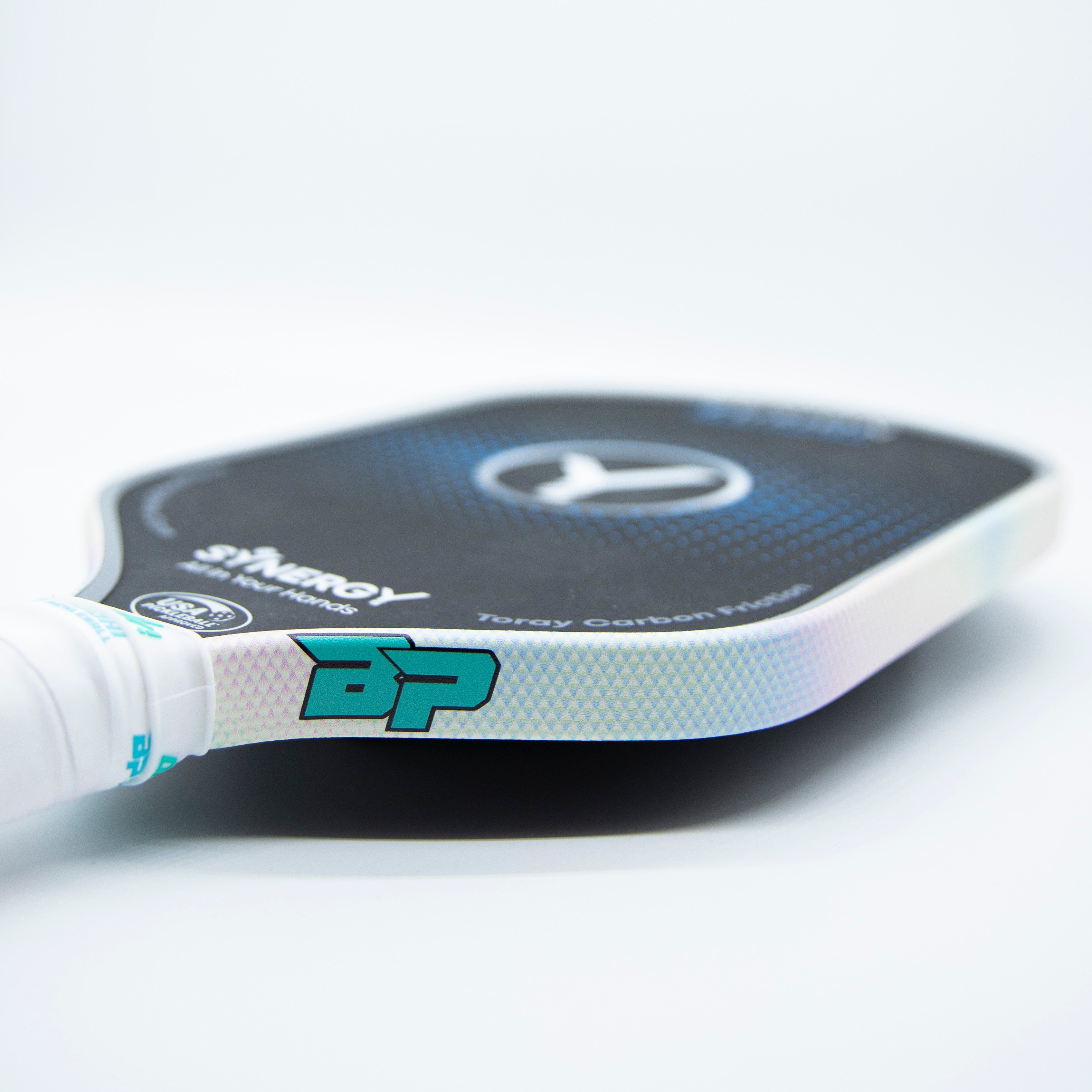 Close-up of a pickleball paddle with a white grip, black face with blue accents, and iridescent edges.