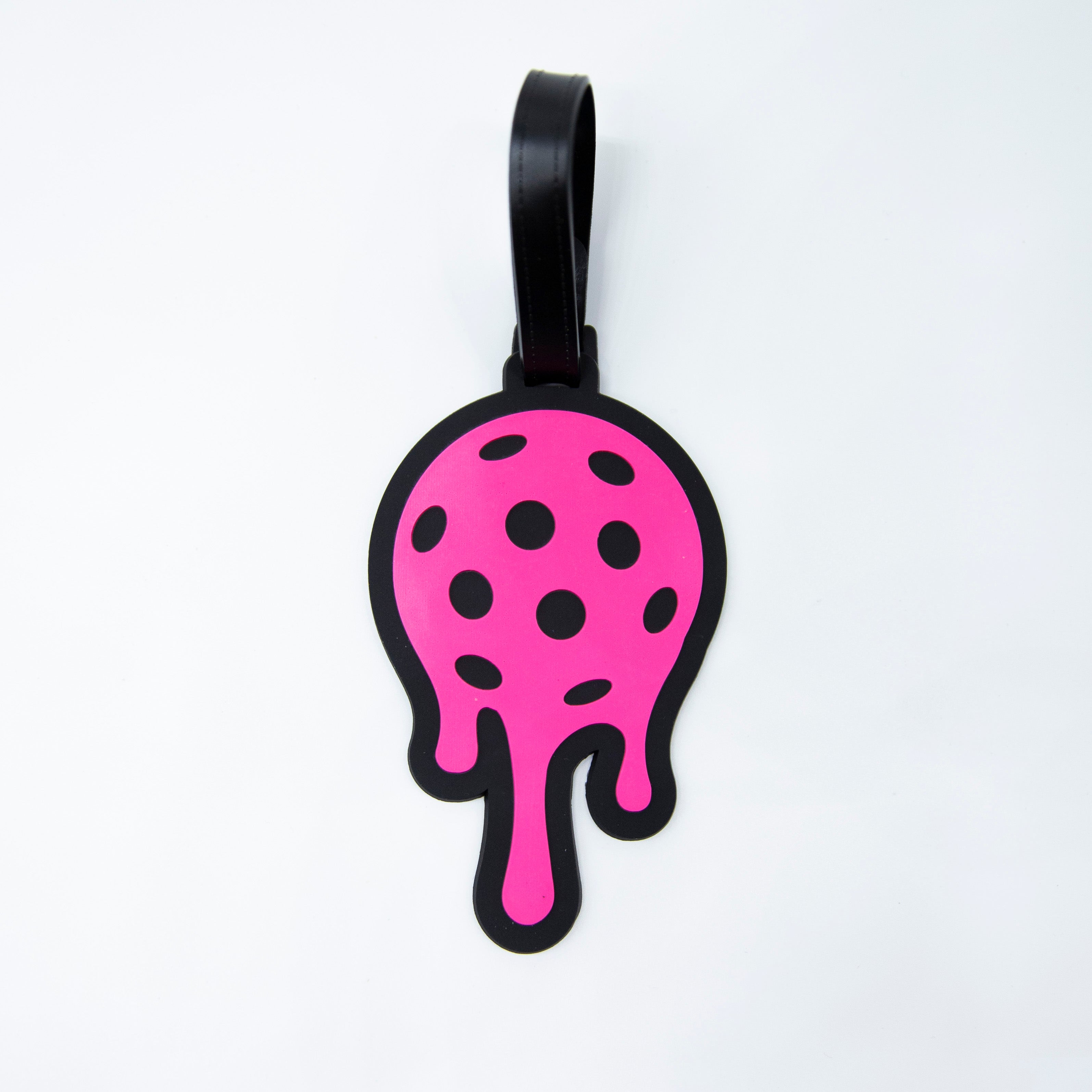 Pink dripping luggage tag with black border and strap on white surface.