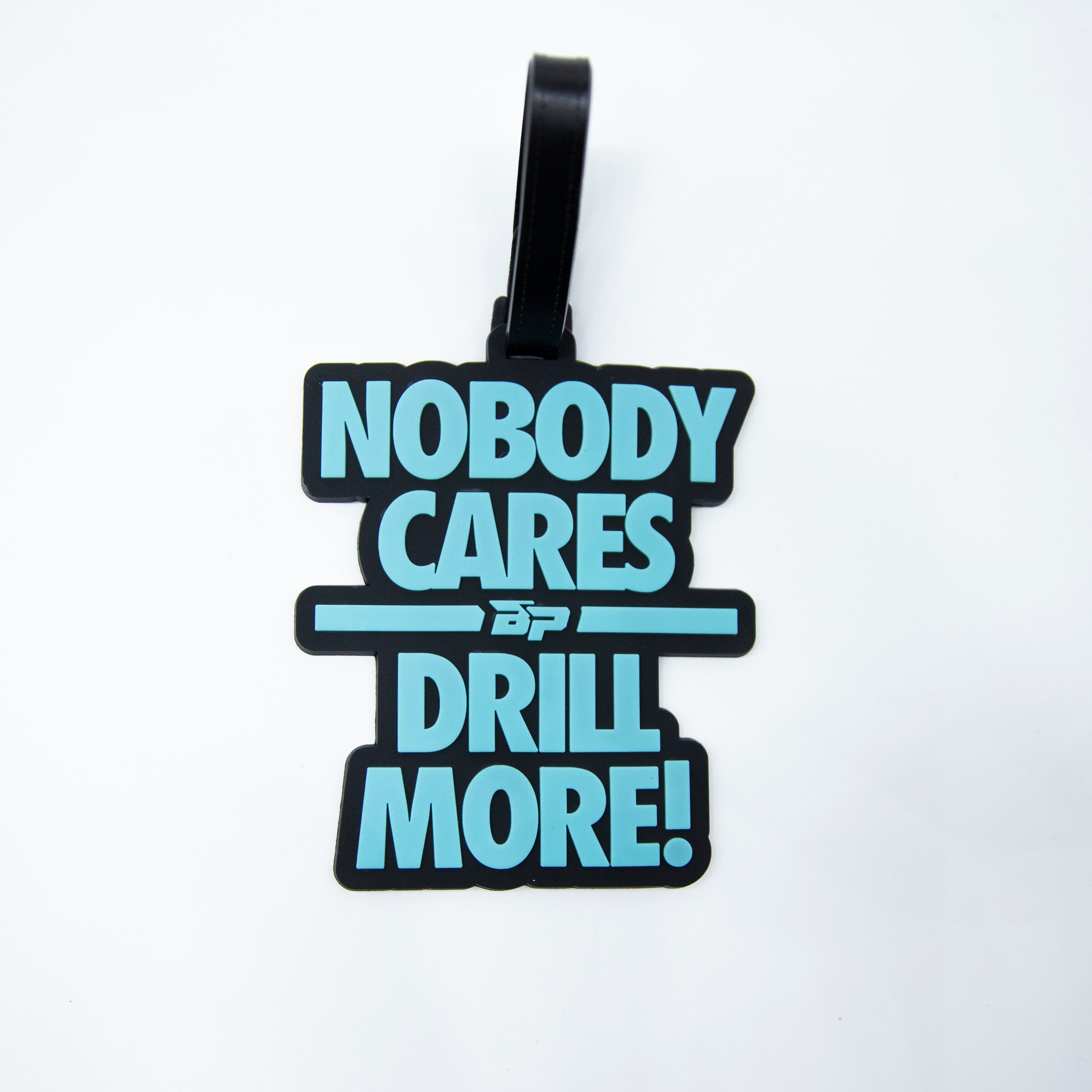 Black luggage tag with blue text "NOBODY CARES DRILL MORE!" and logo.