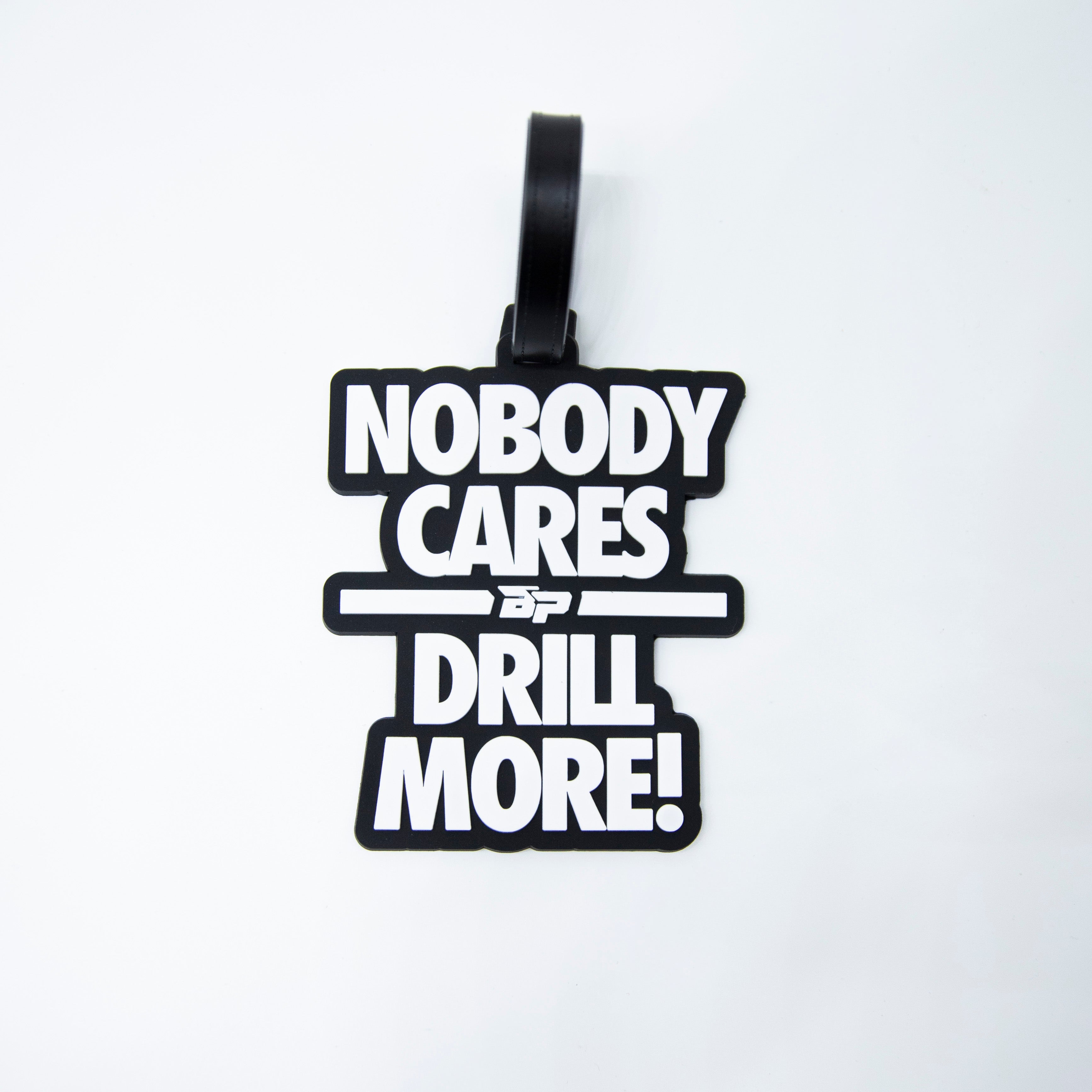A black luggage tag with the words "Nobody Cares Drill More!" in white.