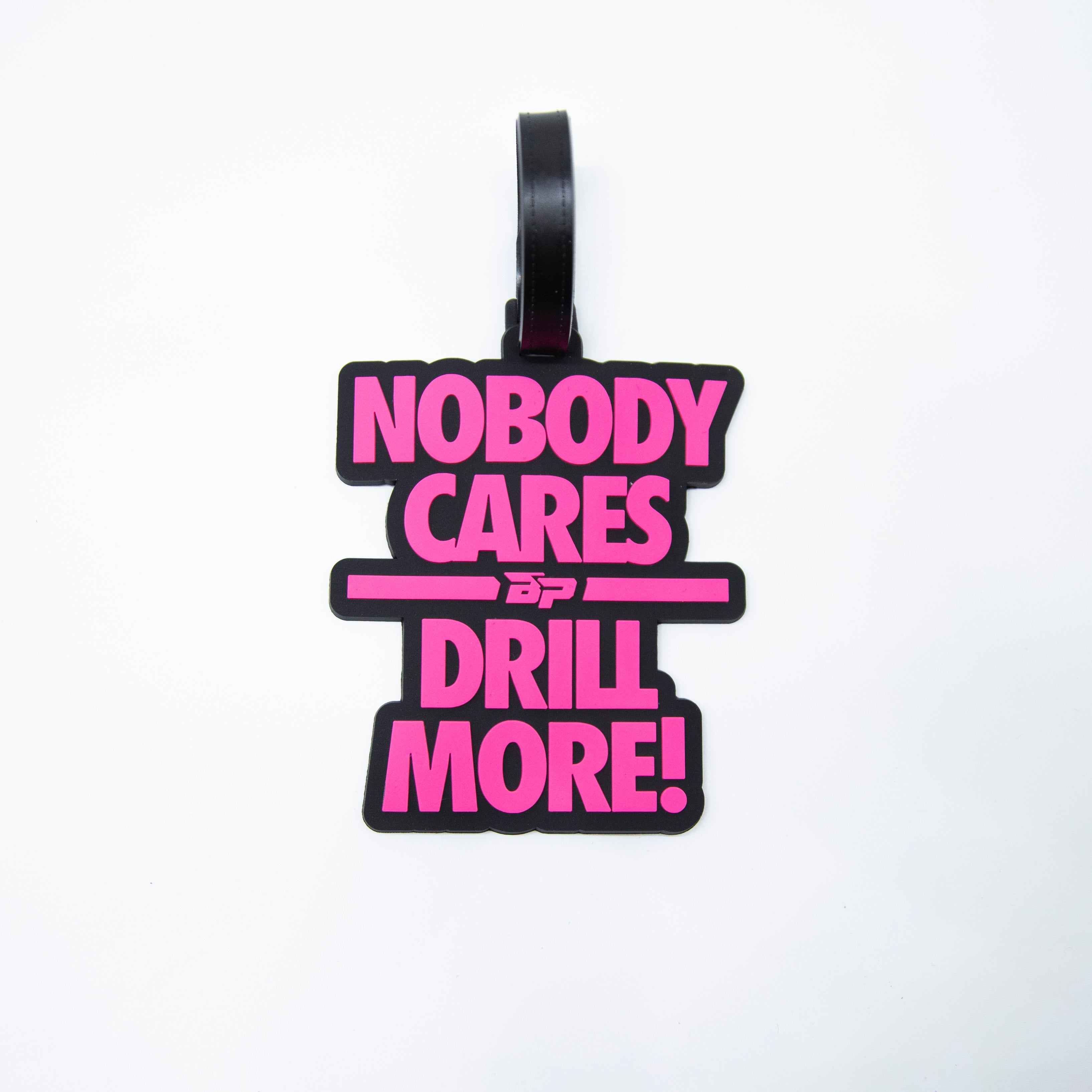 Black luggage tag with pink text: "NOBODY CARES DRILL MORE!"