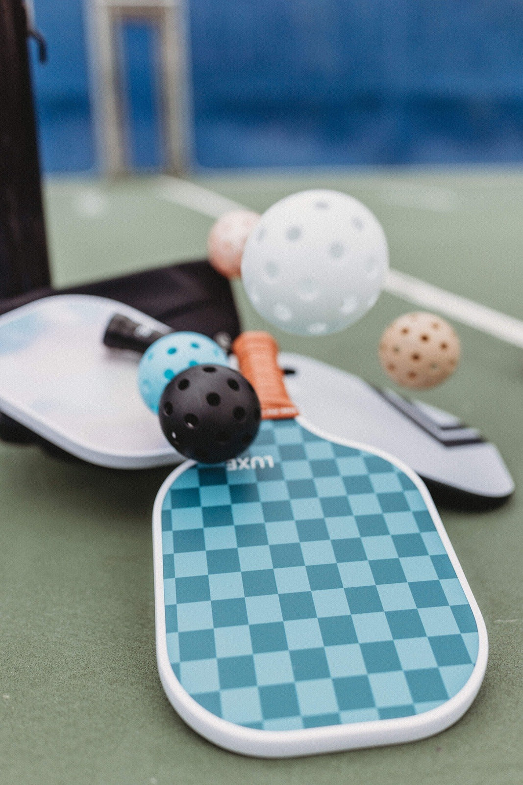 Pickleball equipment on court. Checkered paddle, pickleballs, and bag.