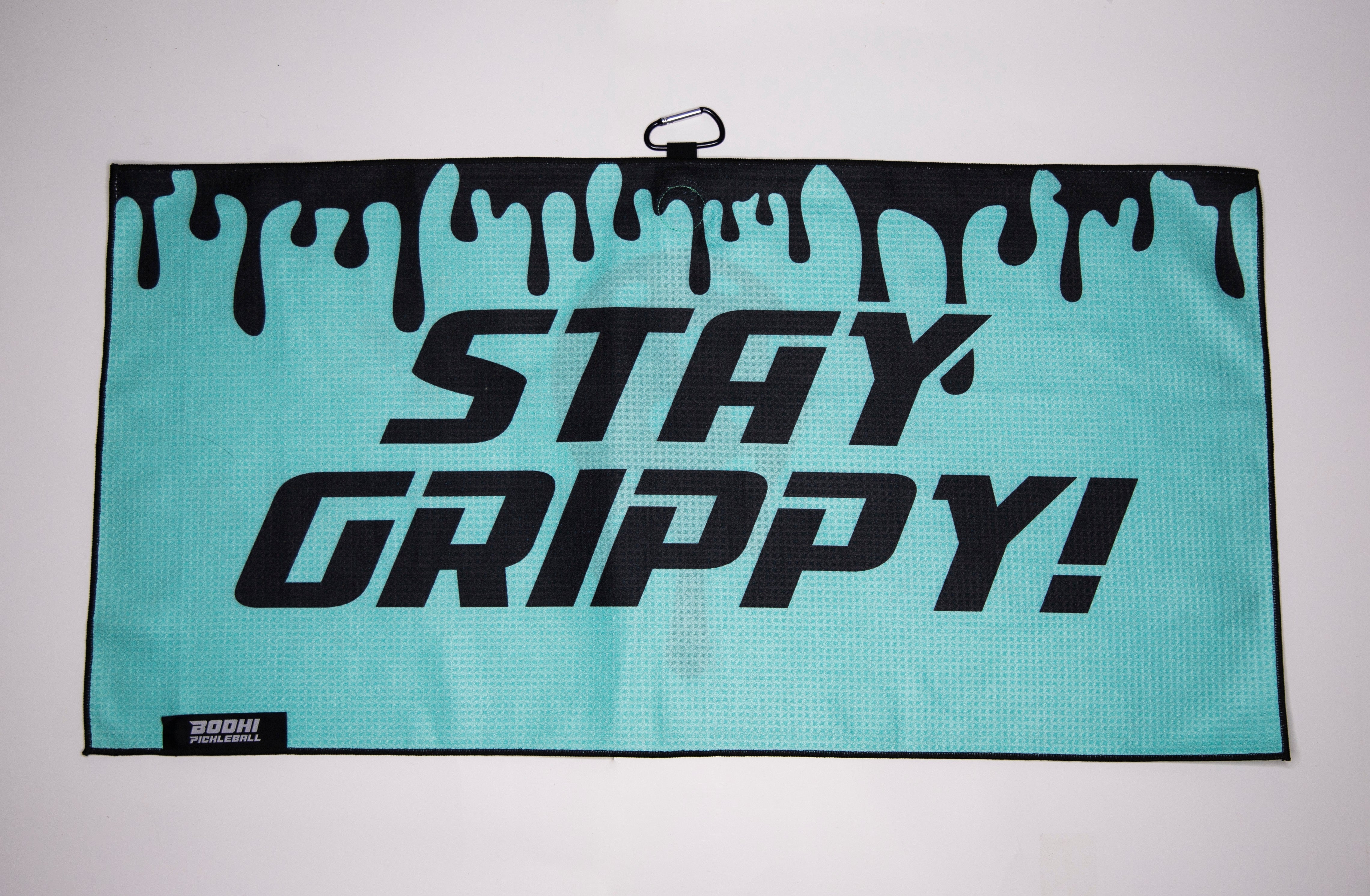 A teal pickleball towel with black text "Stay Grippy!" and dripping black paint design.