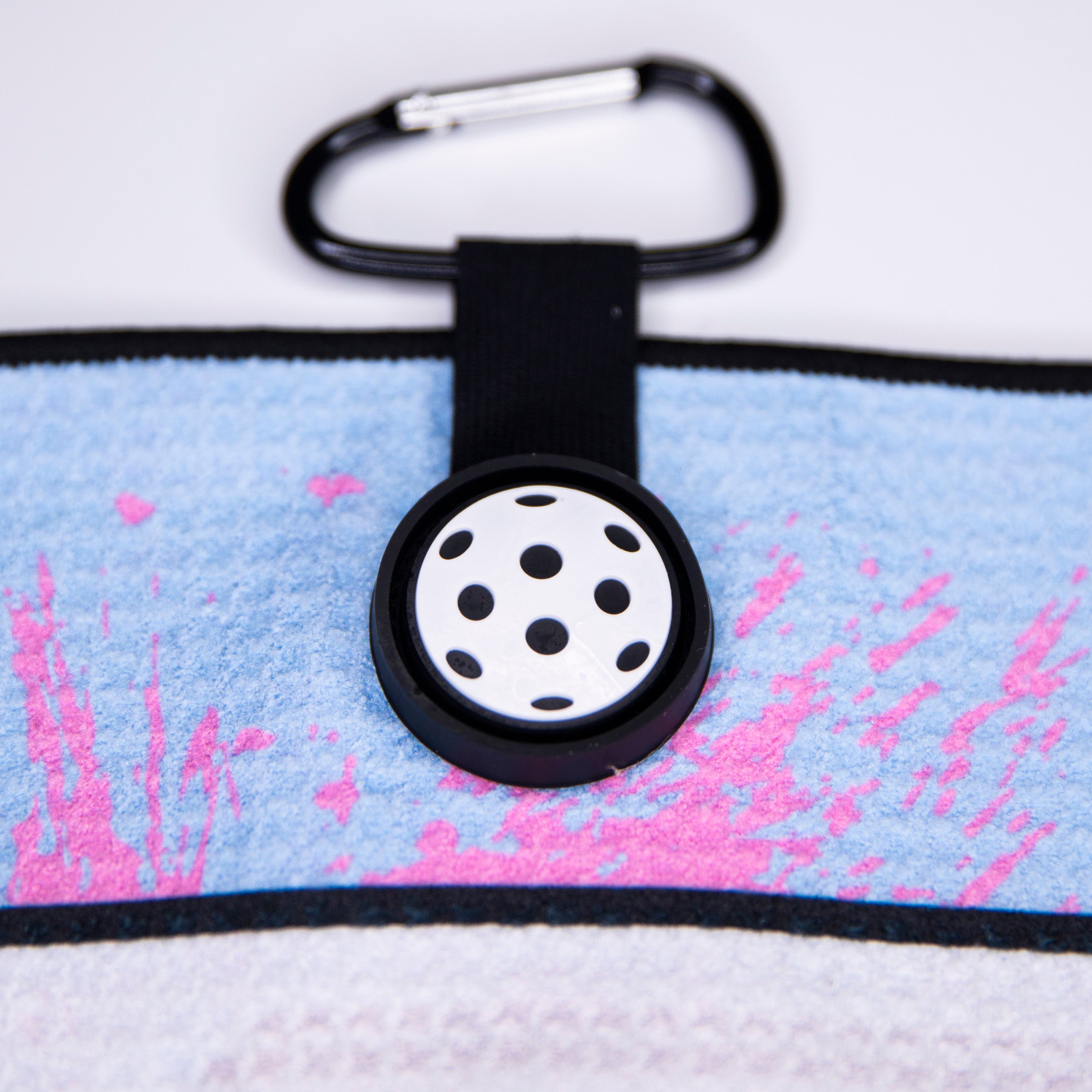 Close up of a patterned towel, black carabiner, and black button with white polka dot pattern.