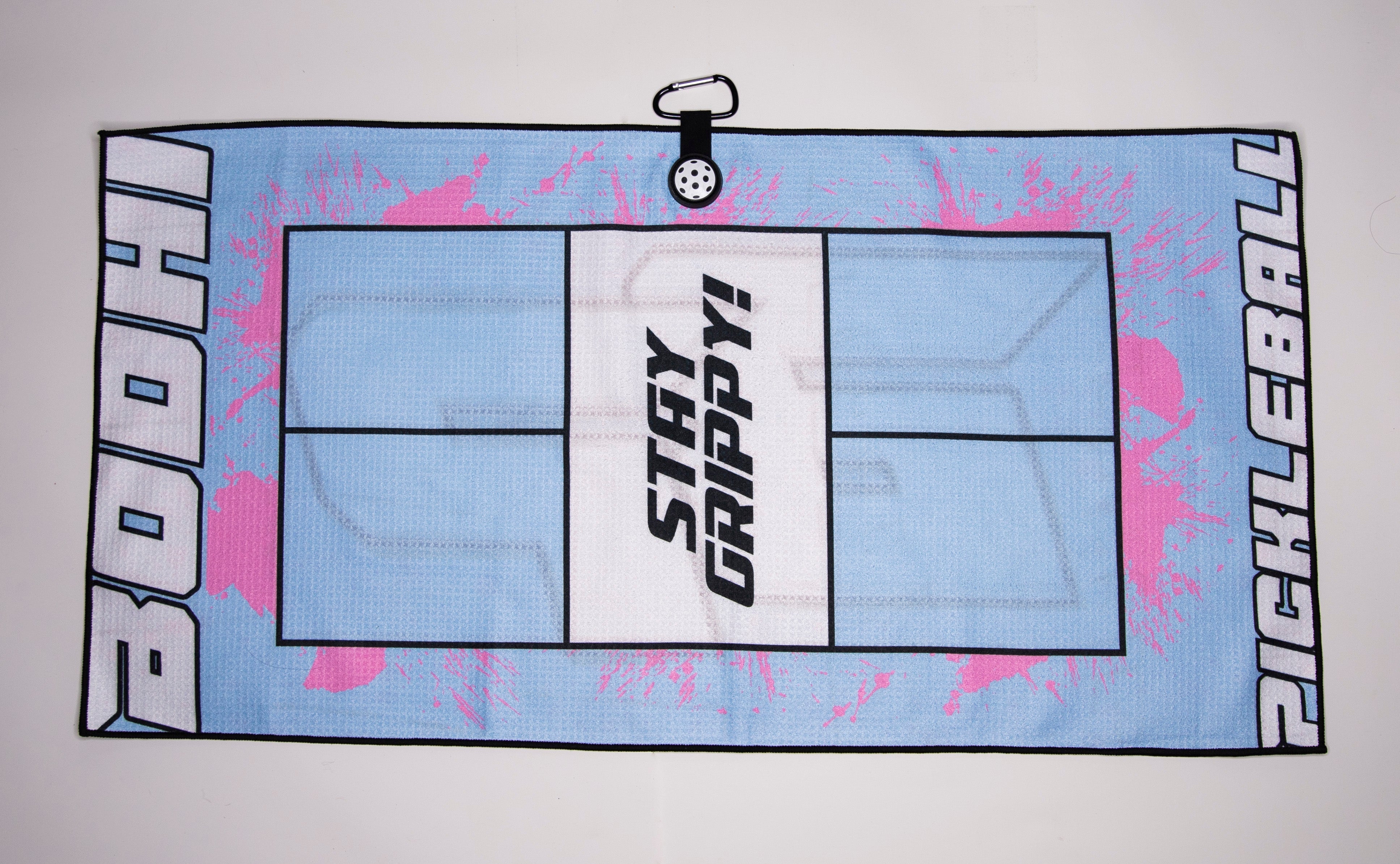 Light blue pickleball towel with pink splatter. It has the word "BODHI" on one side, a pickleball court design in the center, and the word "PICKLEBALL" on the other side. A "stay grippy" design is also featured.