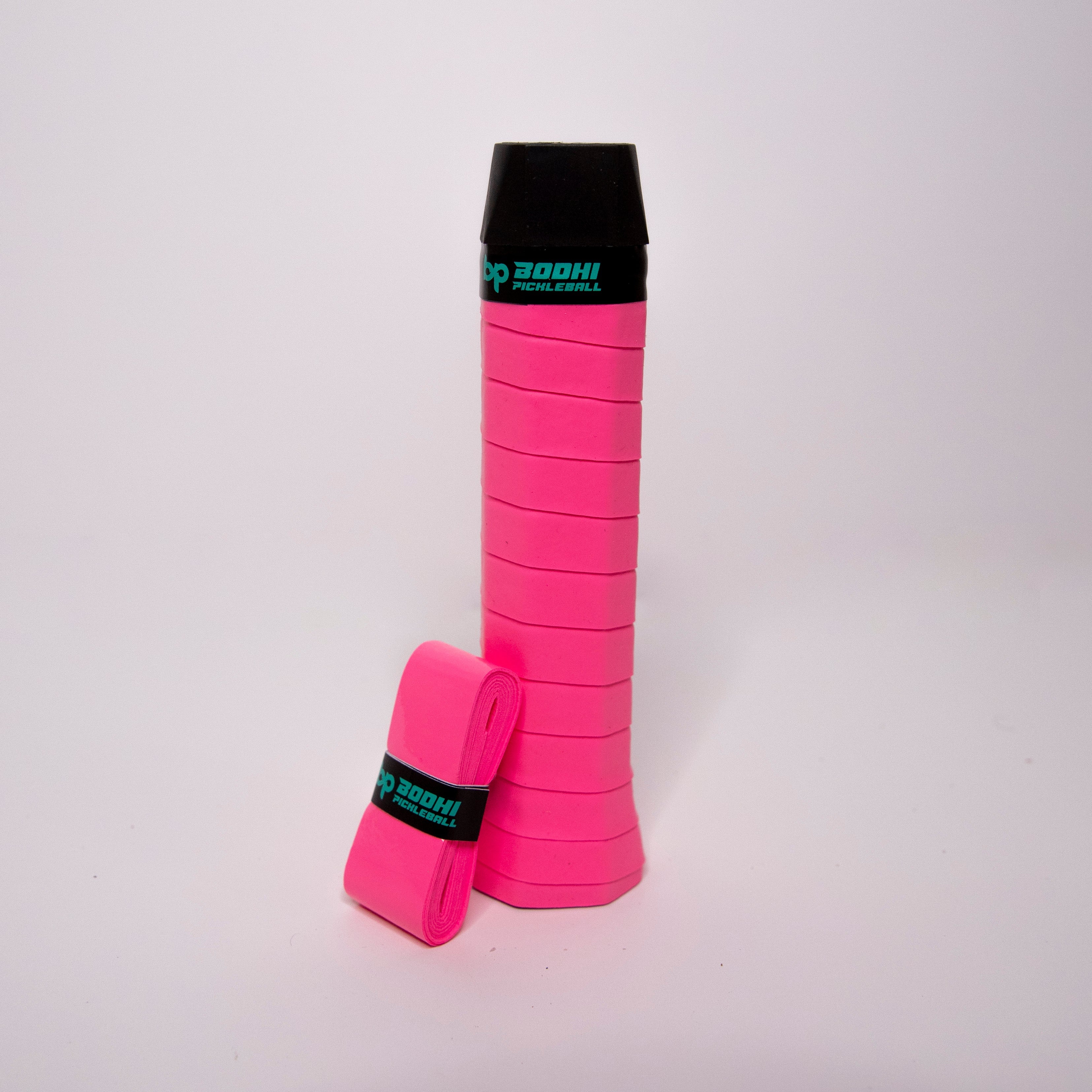A pink pickleball grip and a wrapped pink replacement grip with a black cap sit on a white background.