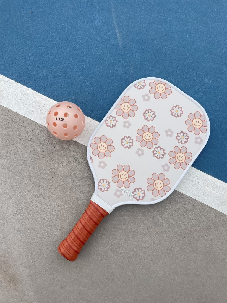 Pickleball paddle and ball with floral design on a tennis court.