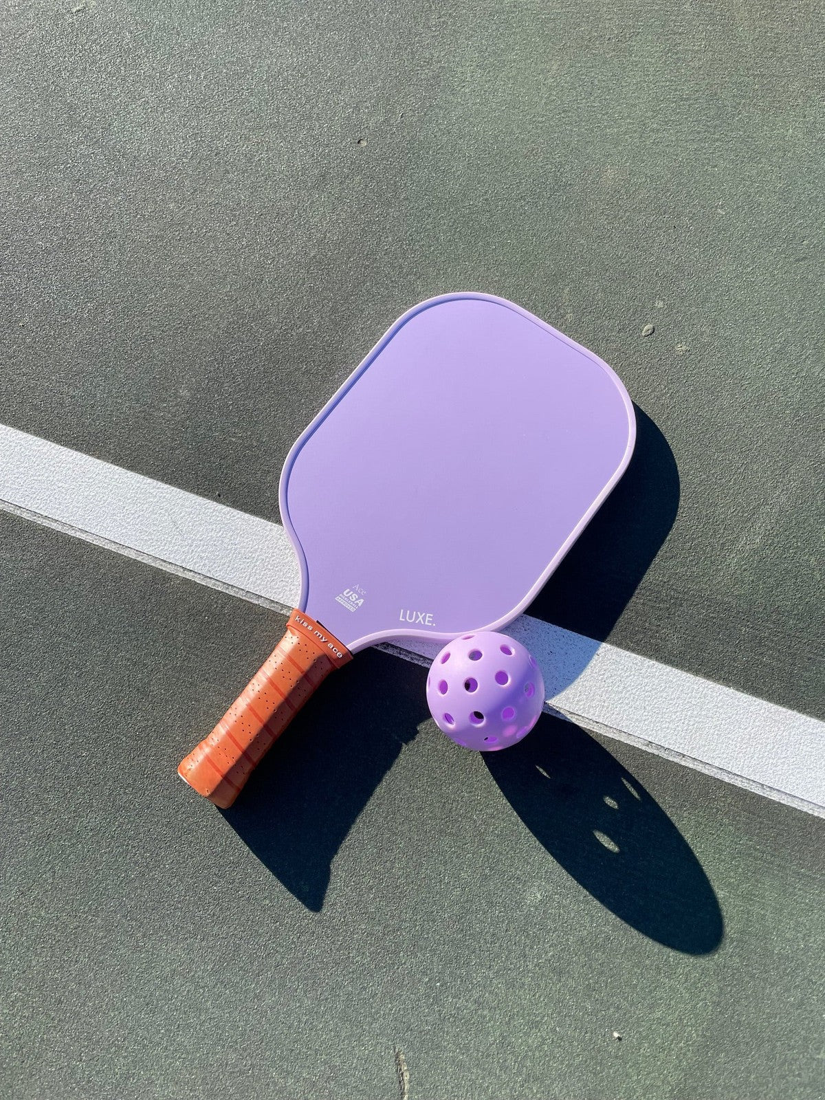 Purple pickleball paddle and ball on green court.