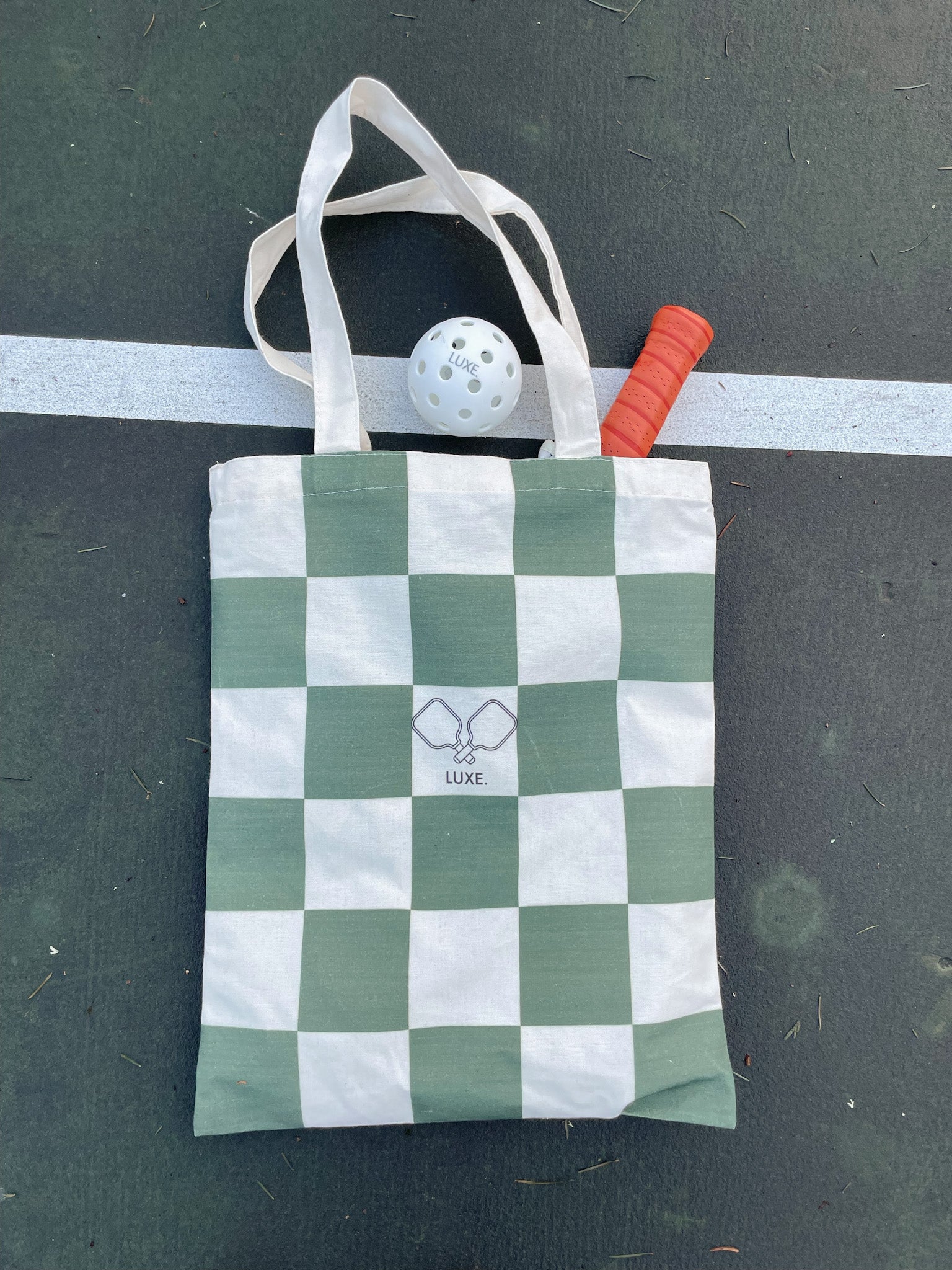 Checkered tote bag with pickleball ball and paddle on a tennis court.